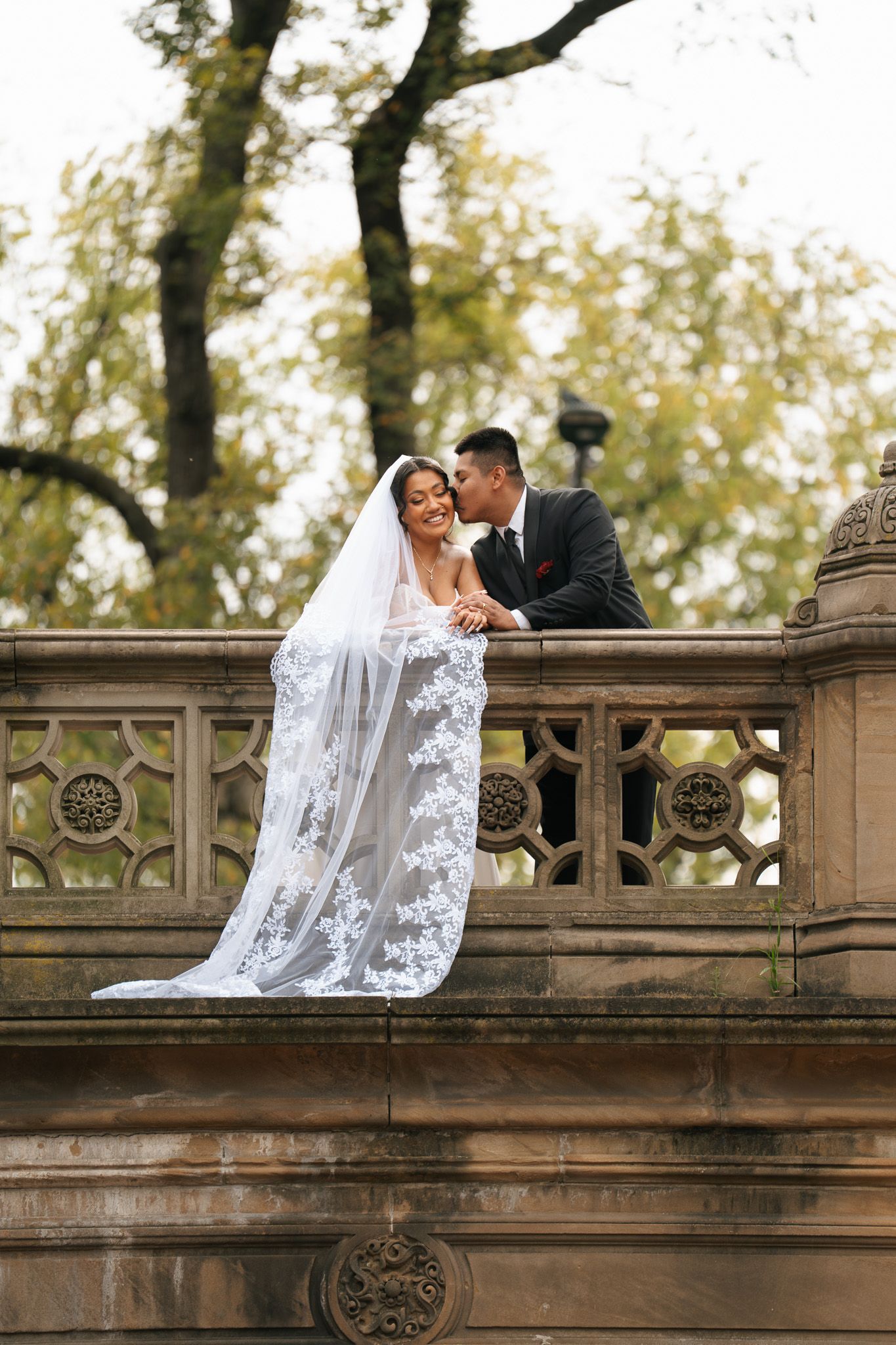 Romantic moment on an ornate stone bridge with lace veil flowing.