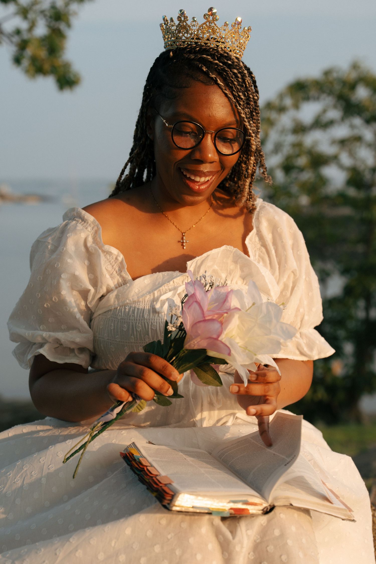 Person in white dress with crown reading while sitting outdoors.