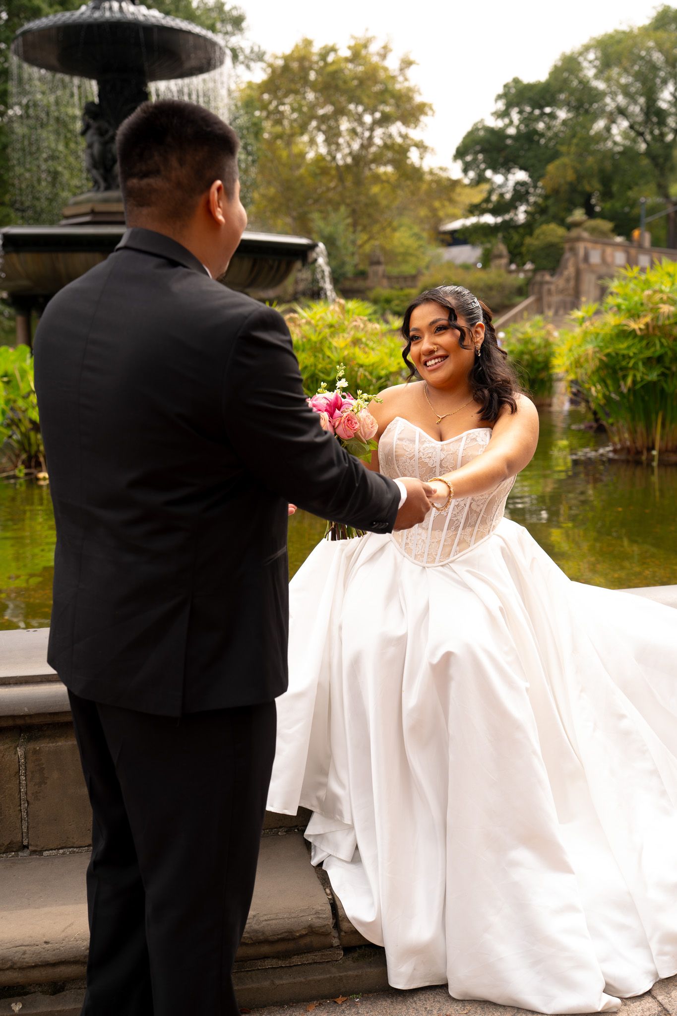 Wedding couple in formal attire posing by a lake with flowing white dress.