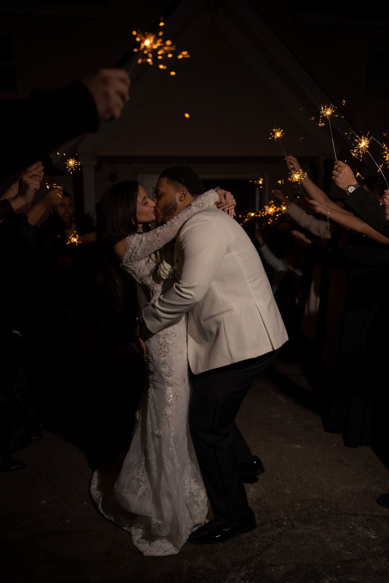 A couple dances together at a wedding reception with sparklers glowing in the dark background.