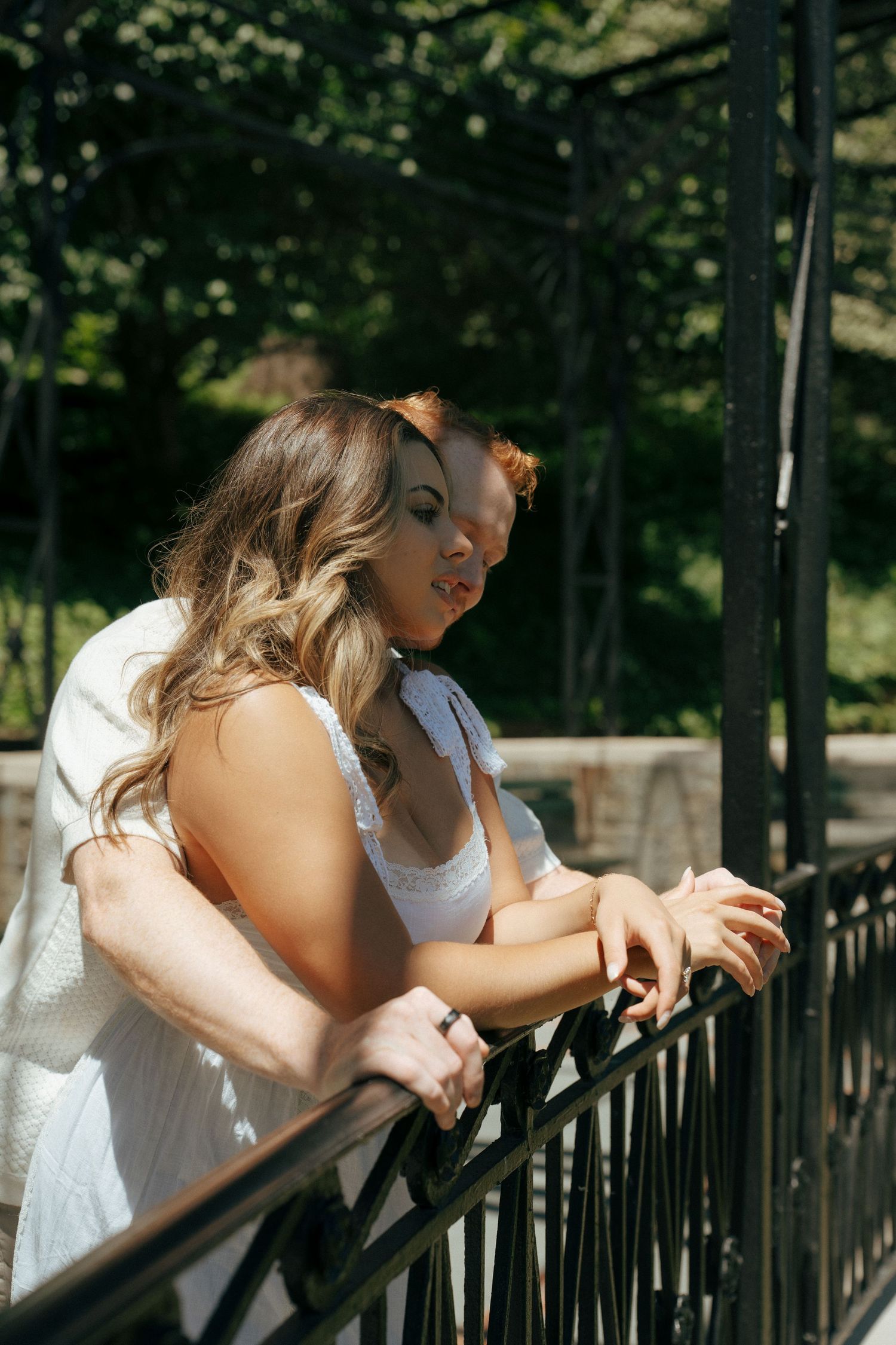 Couple leaning on a metal railing together in dappled sunlight.