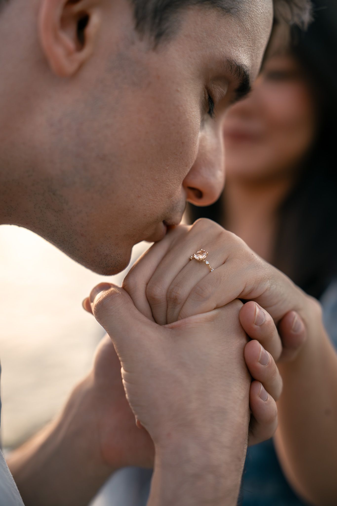 Close-up shot of hands being kissed tenderly against a dark background.