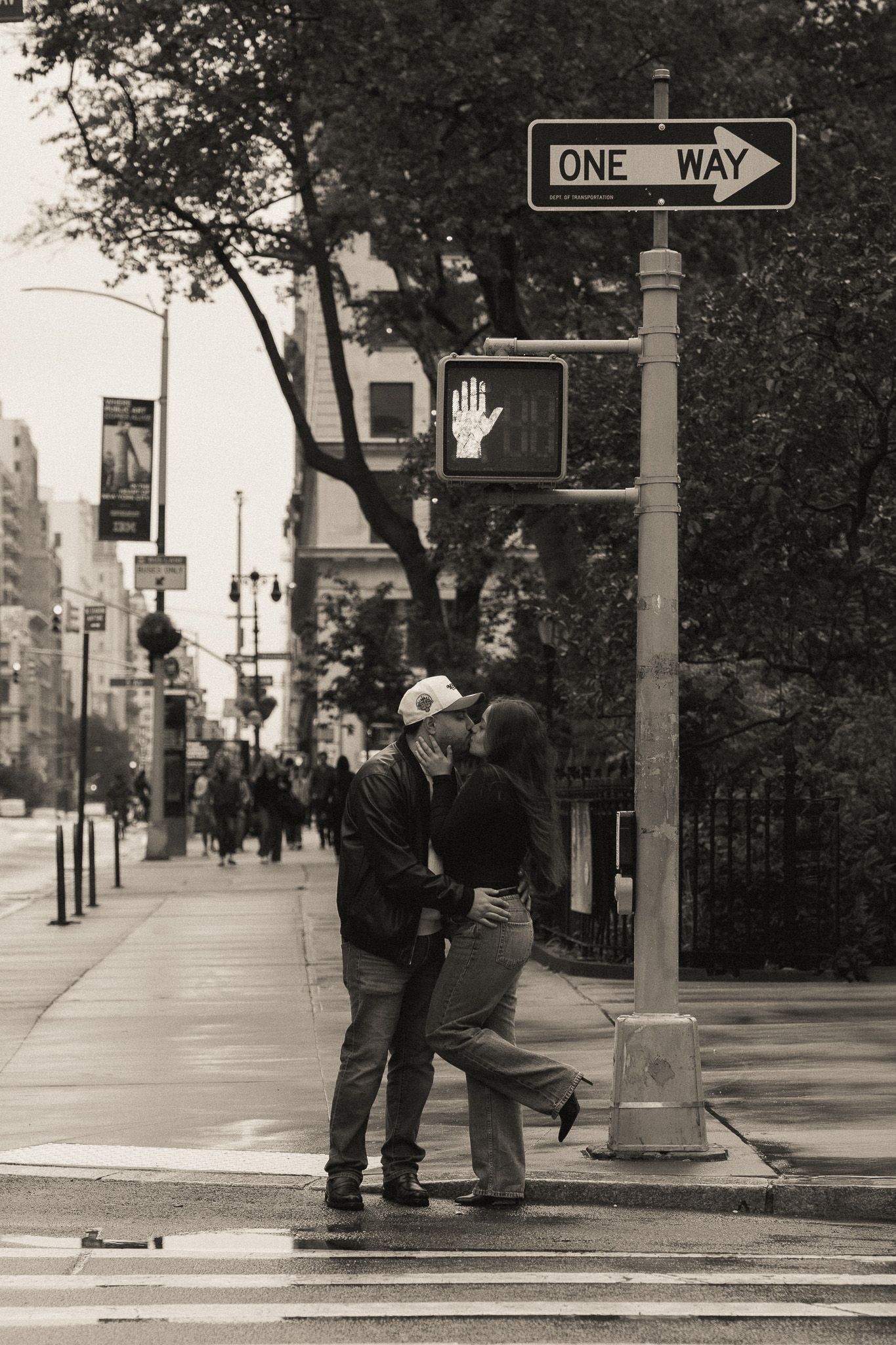 Black and white street scene with people walking near a one way sign on a city sidewalk.