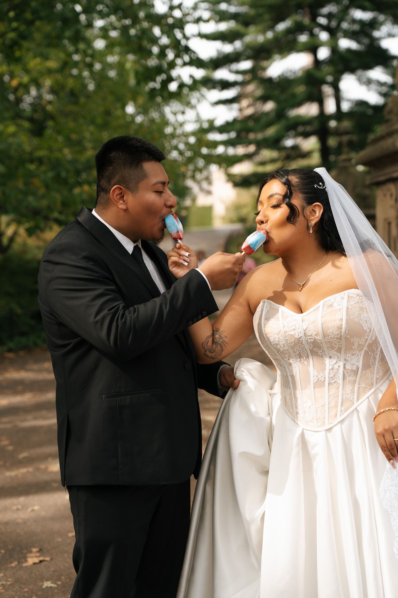 A bride and groom playfully feed each other candy during their outdoor wedding photo session.