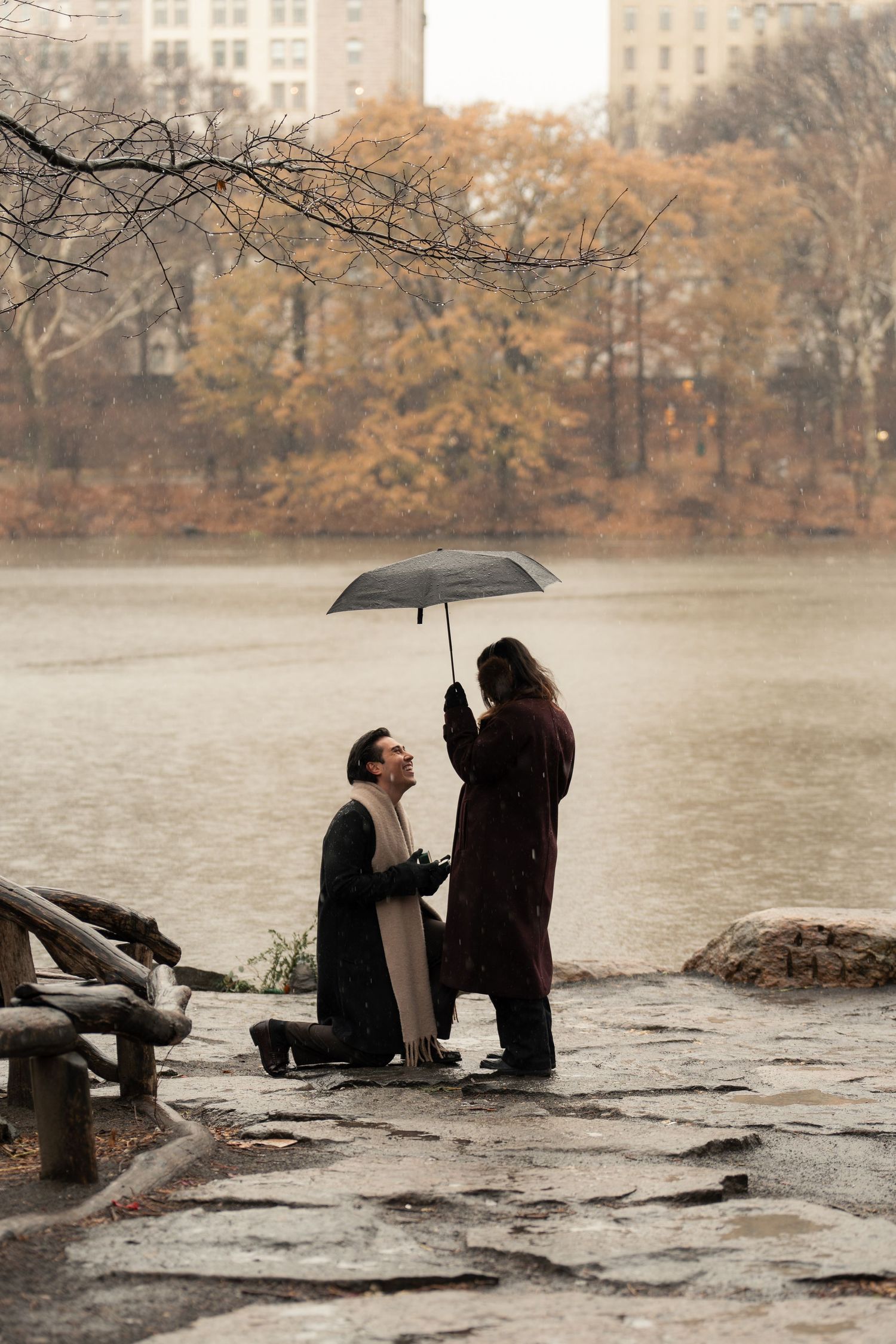 A series of photos showing two people sitting on rocks by a lake during autumn with an umbrella.