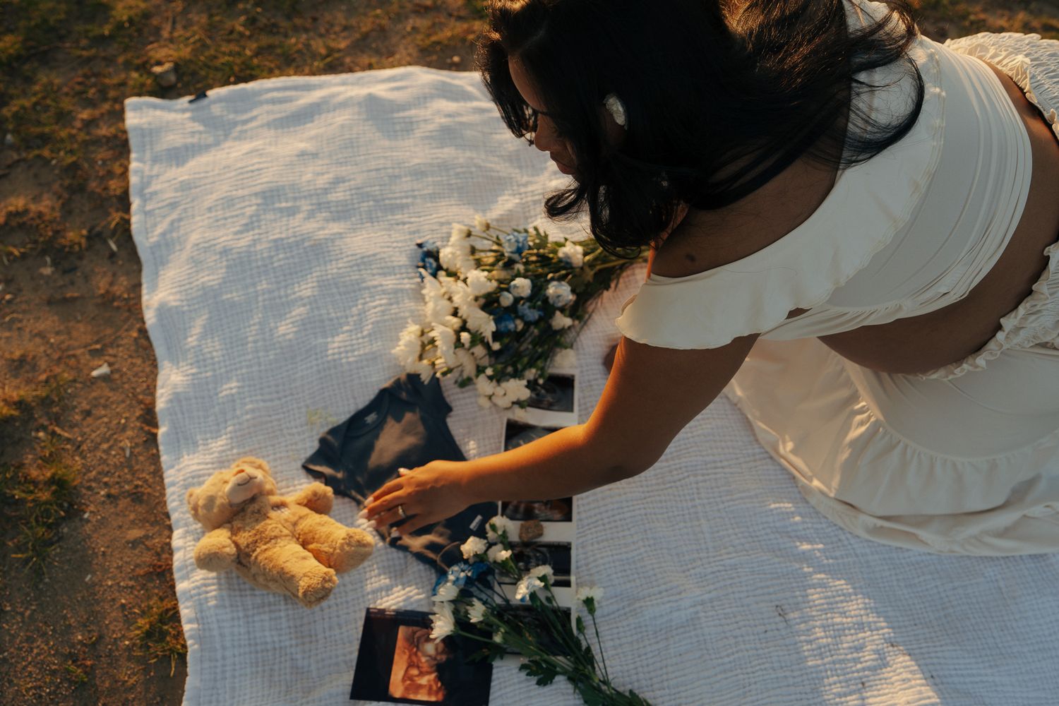 Intimate maternity photoshoot with flowers and white dress on grassy shore.