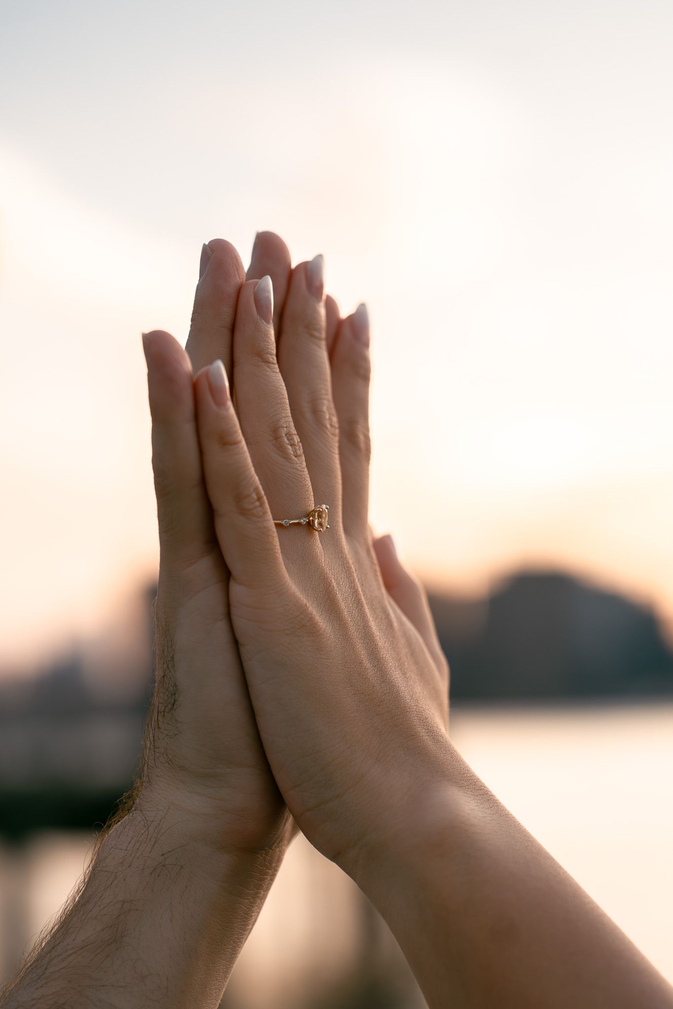 Hands raised against sunset sky showing engagement ring in silhouette.