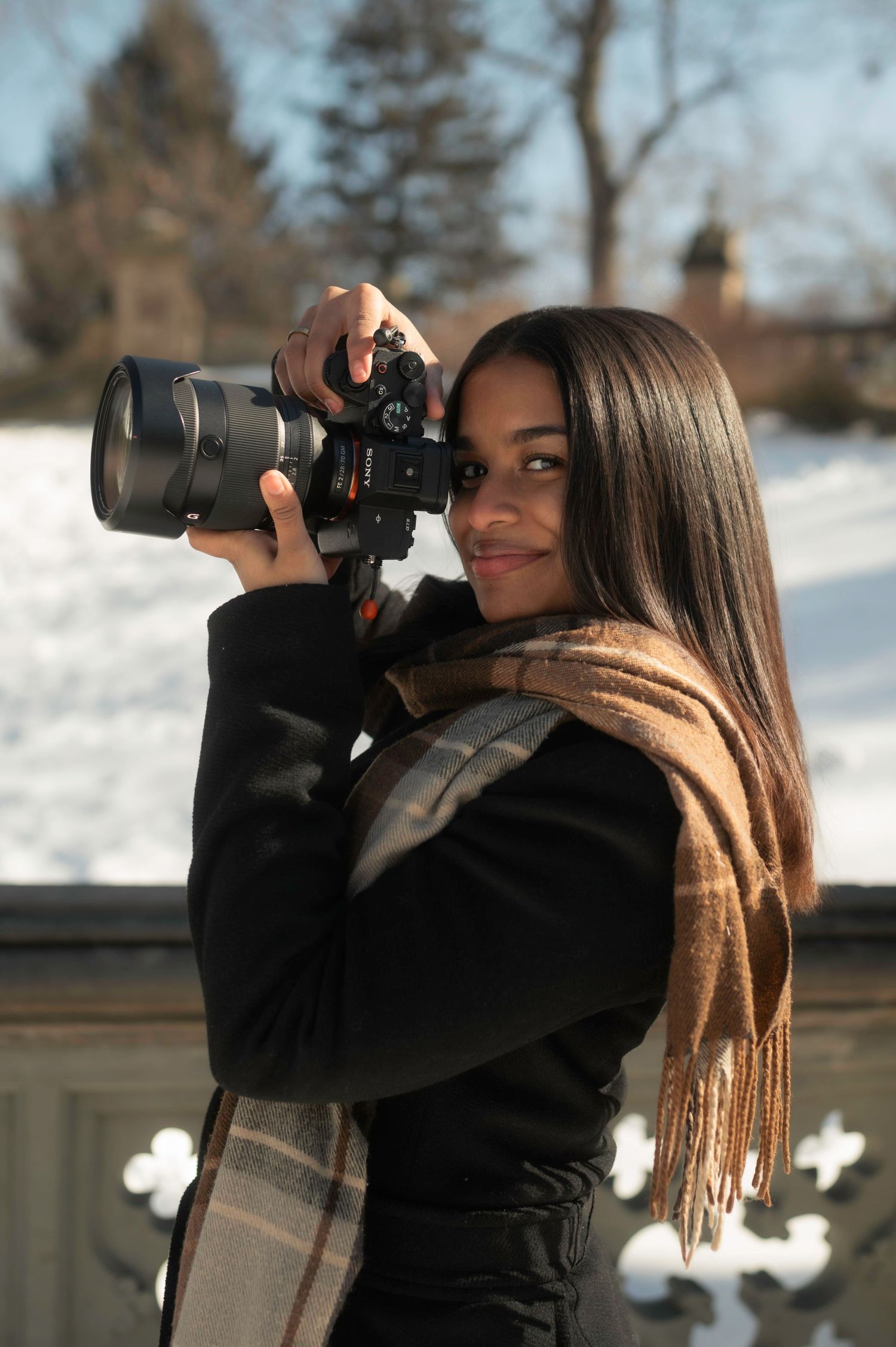 Photographer with long hair taking pictures with a telephoto lens camera in a winter outdoor setting.