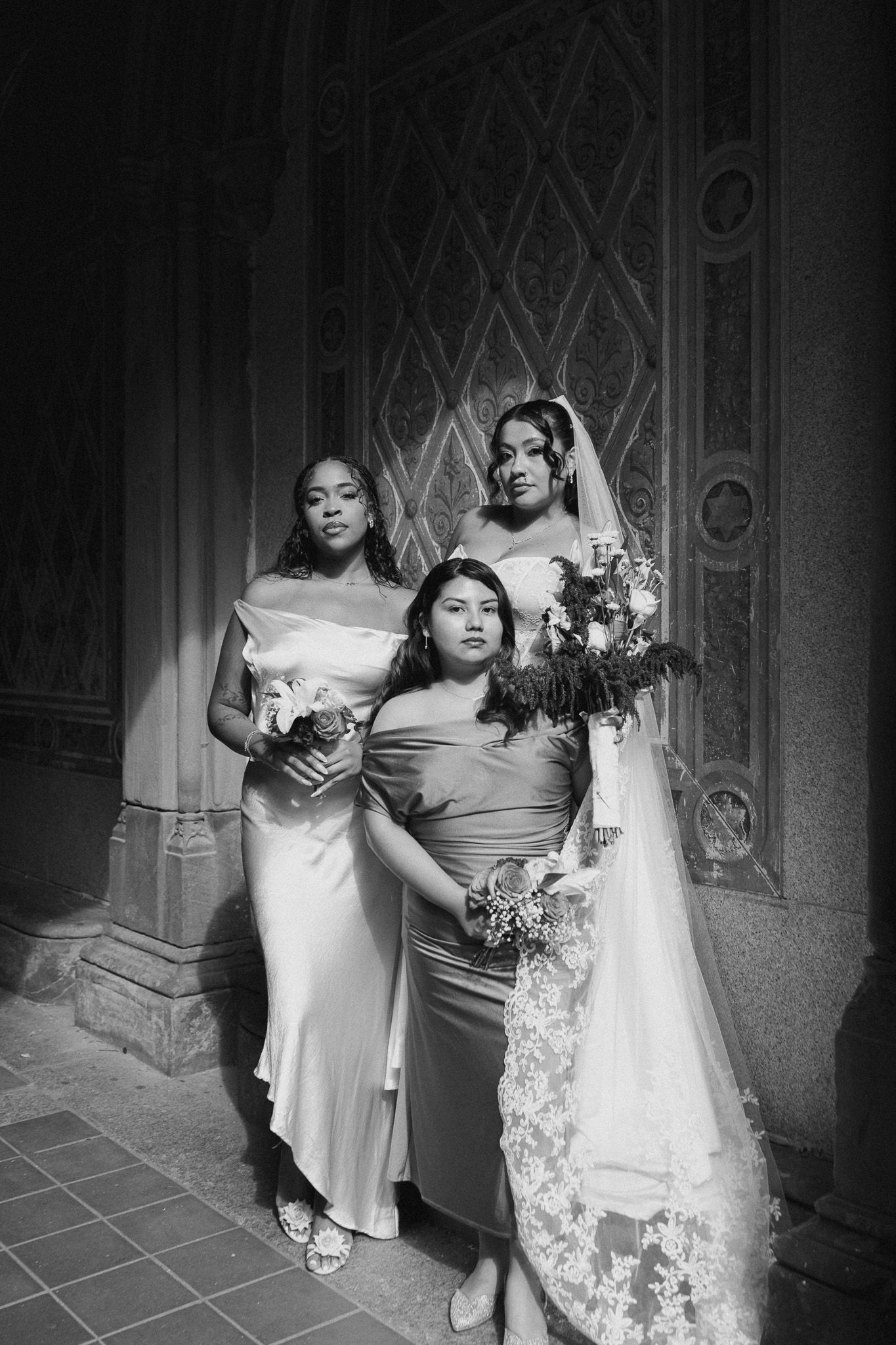 Elegant bridal party in black and white poses against ornate architectural backdrop with bouquets and flowing dresses.