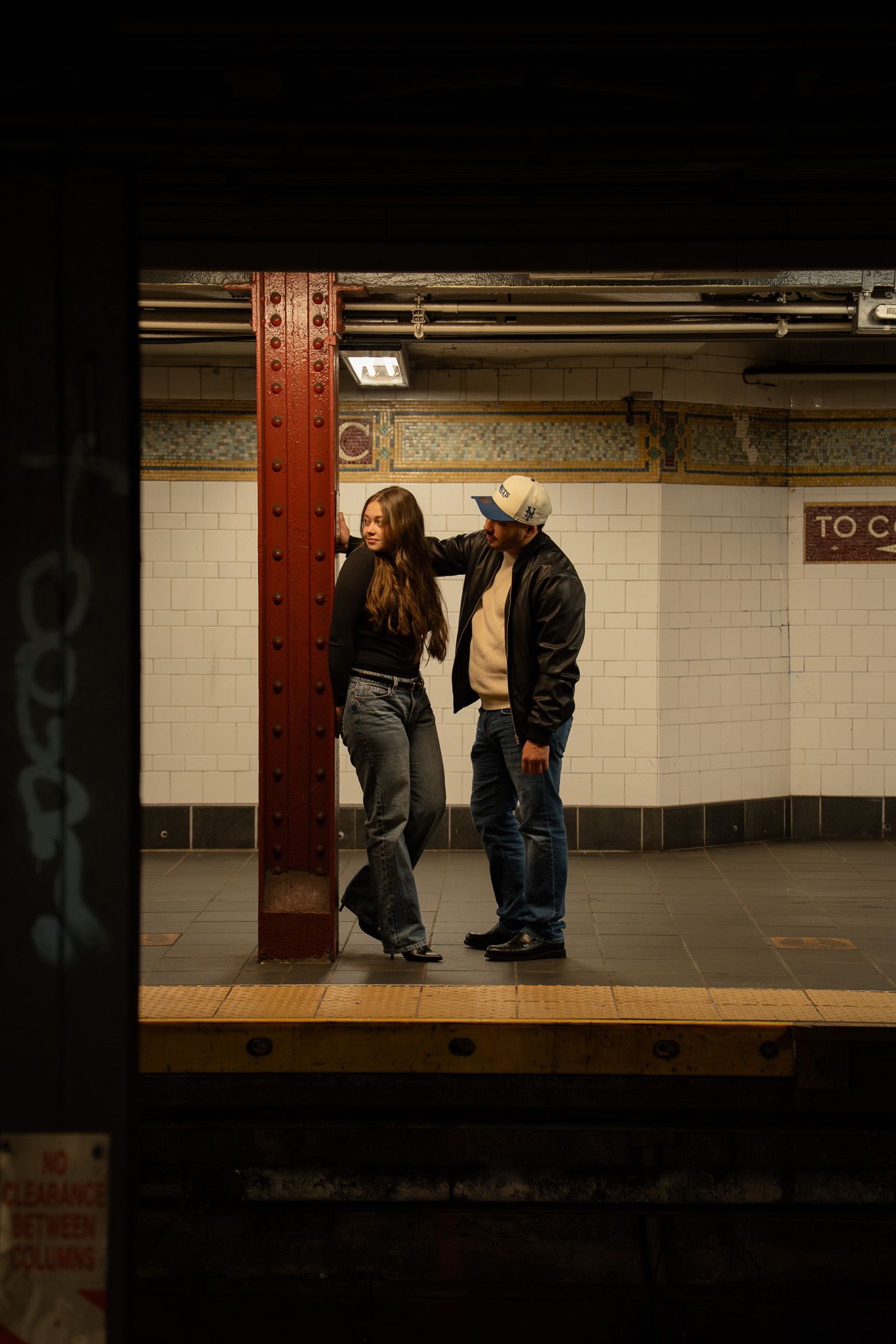 Silhouettes of people standing in a dimly lit subway station with white tiled walls.