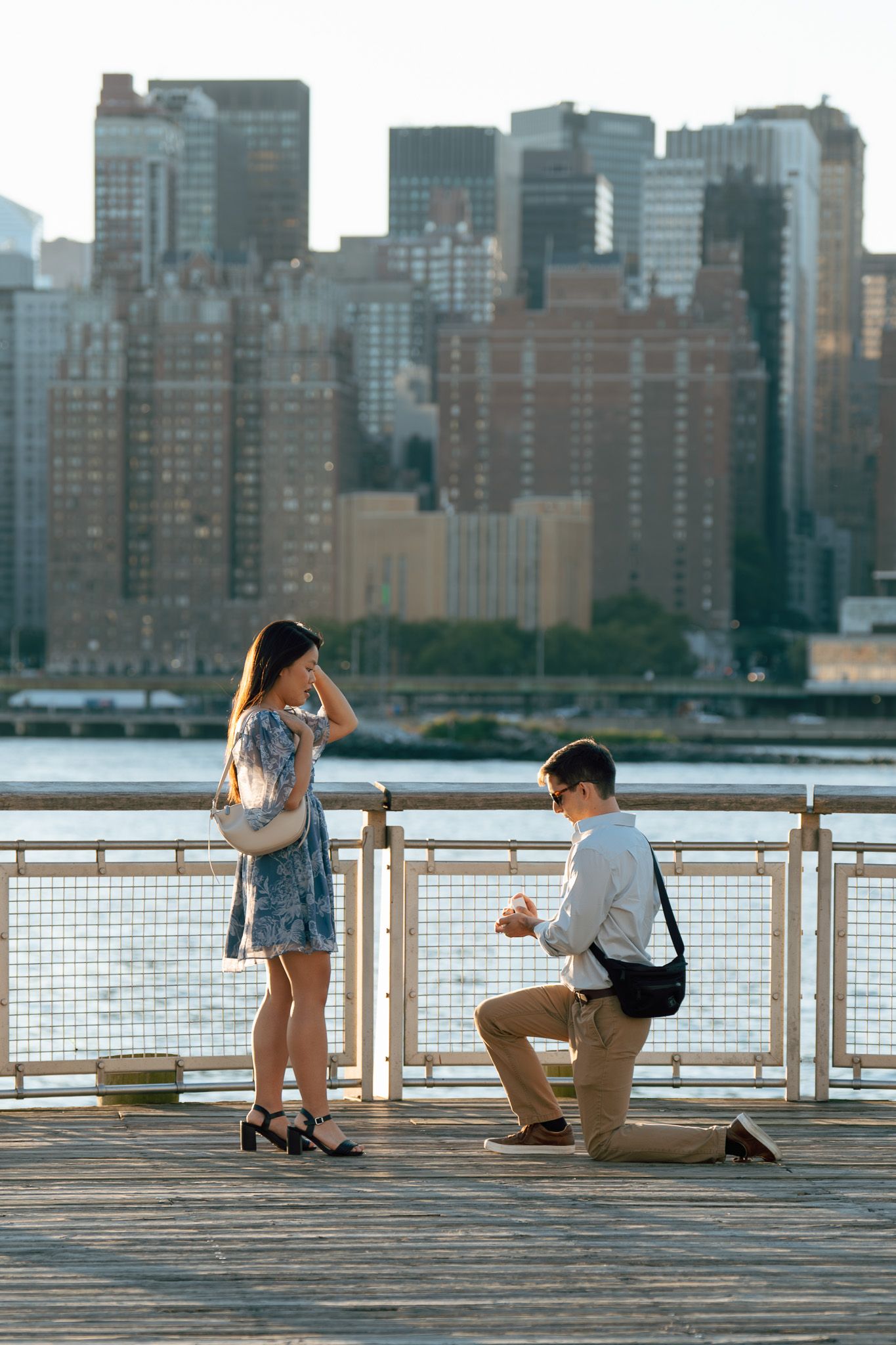 Romantic proposal on waterfront deck with Manhattan skyline in background.