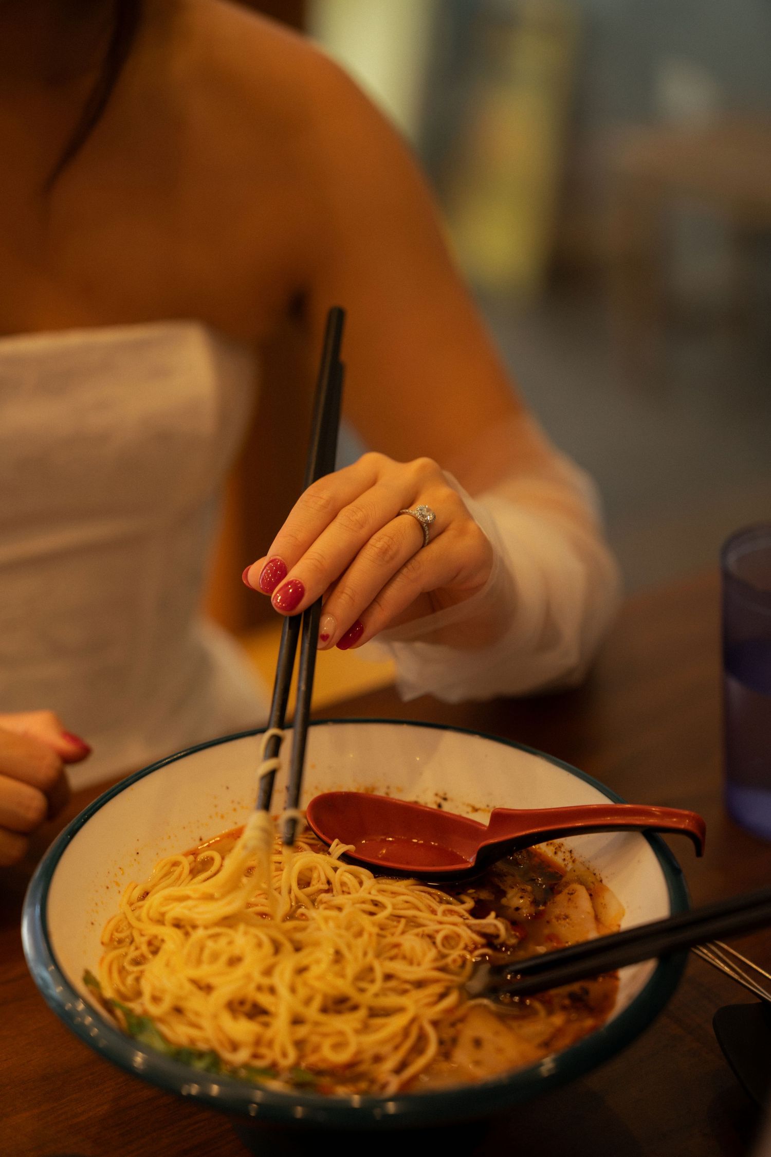 Woman with red nails eating noodles with chopsticks from a large bowl at a restaurant.