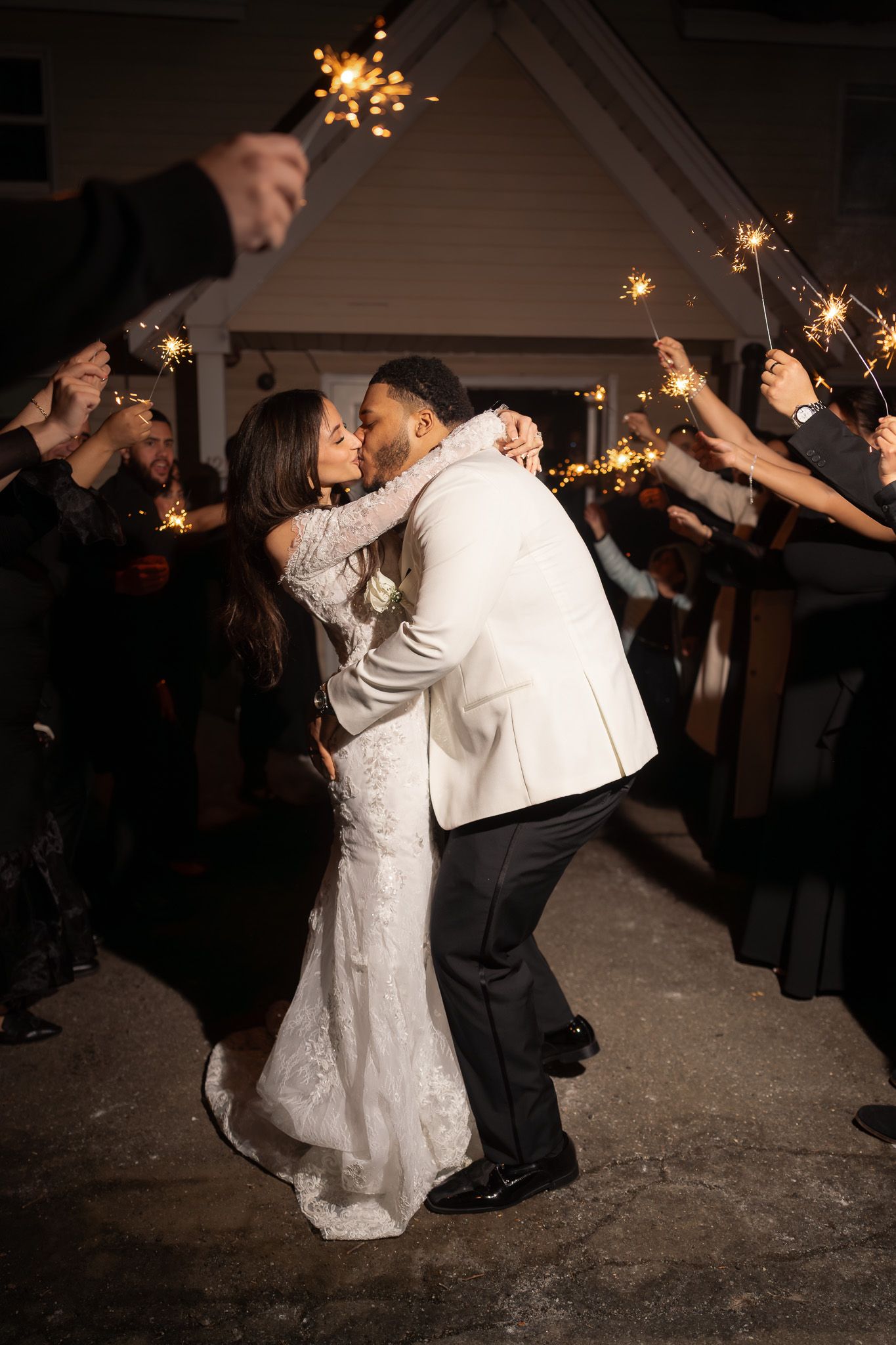 Bride and groom share a romantic kiss during a sparkler send-off at their outdoor wedding reception at night.