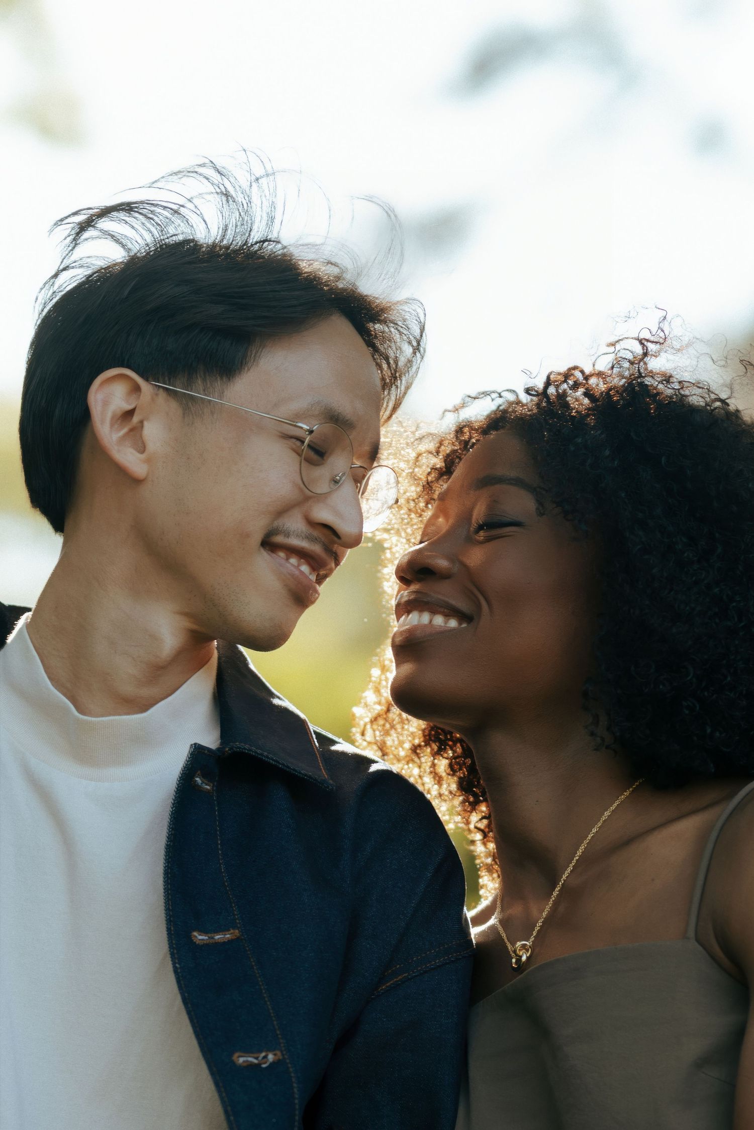 Happy interracial couple smiling and leaning foreheads together outdoors in soft natural light.
