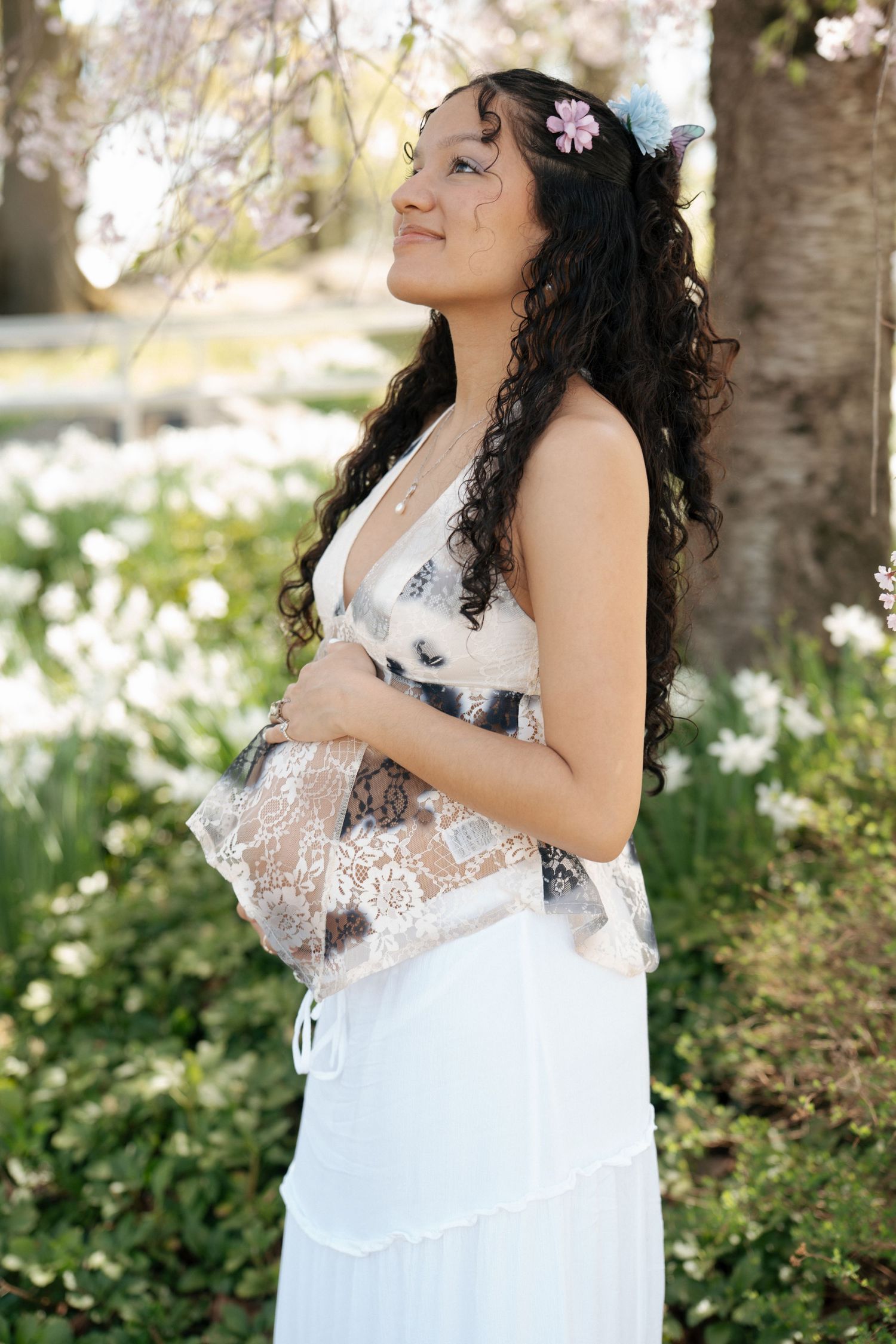 A person in a white lace dress poses in a garden with blooming spring flowers.