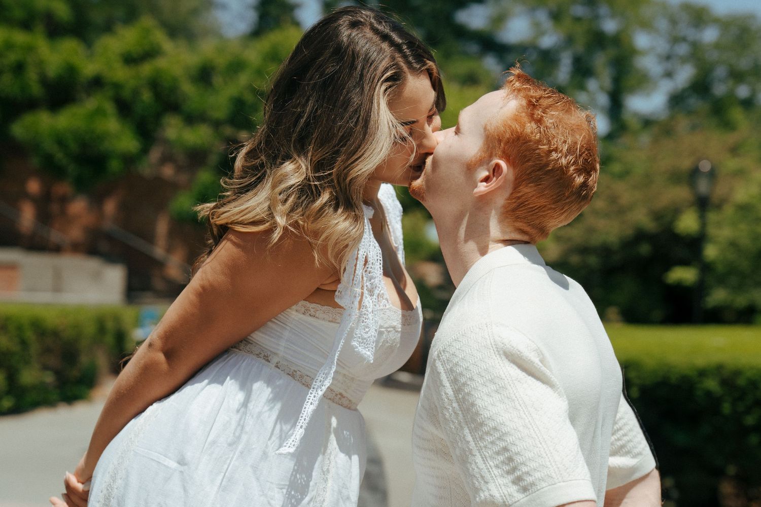 Couple in white clothing sharing romantic moments in a sunny garden setting.