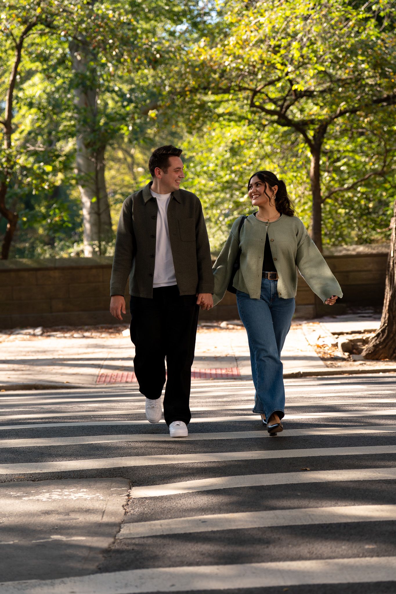 A couple walking together on a tree-lined path in autumn with dappled sunlight.