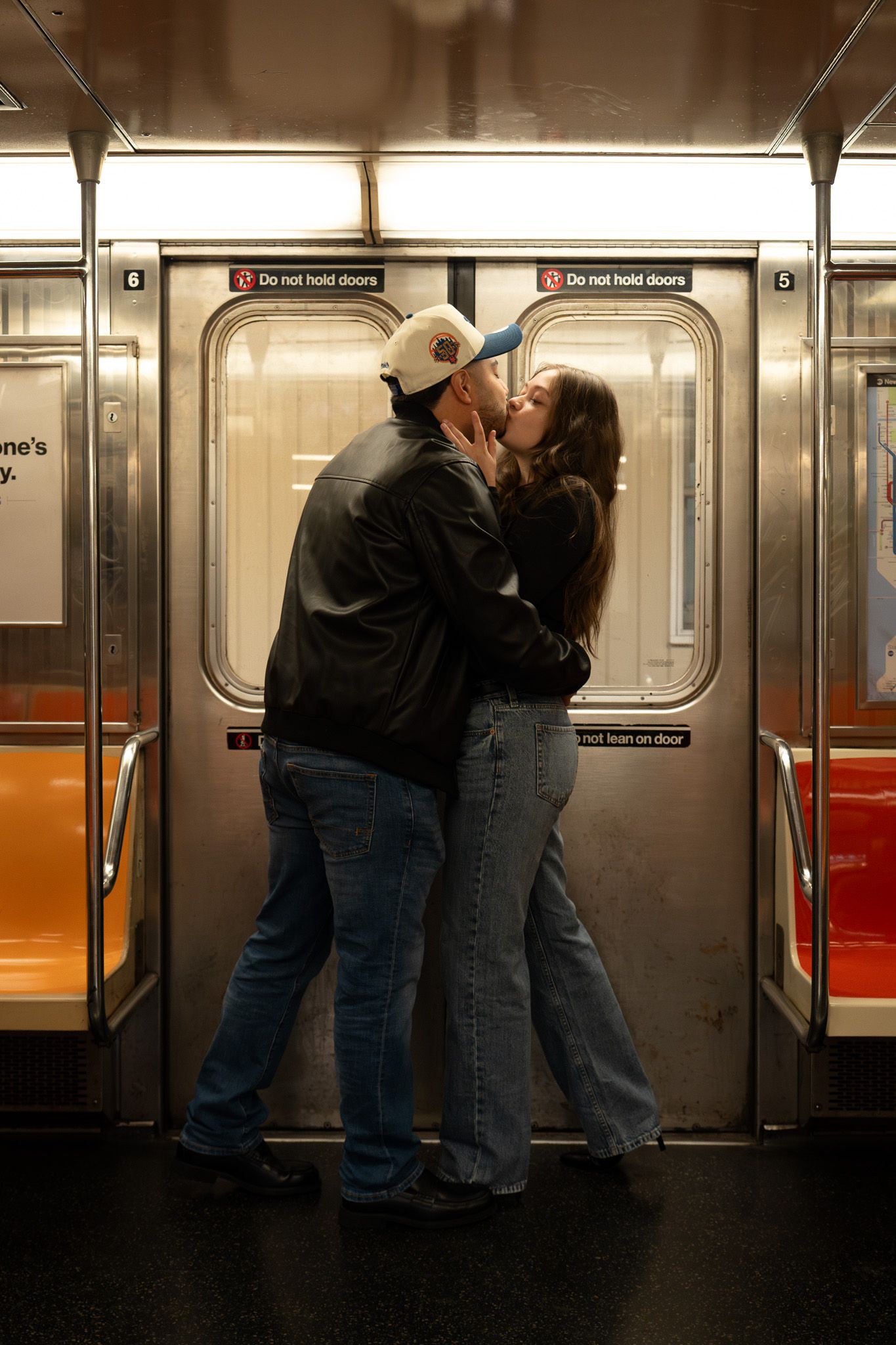 Romantic couple embrace against subway car doors in dimly lit train.
