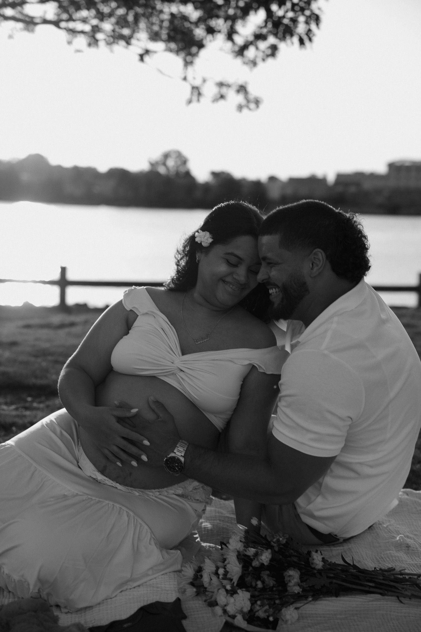 Couple embracing on blanket during sunset with water and trees in background.