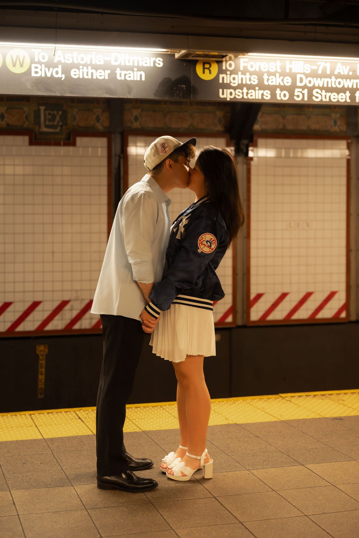 Couple kissing on a New York City subway platform beside the W and R train signs.