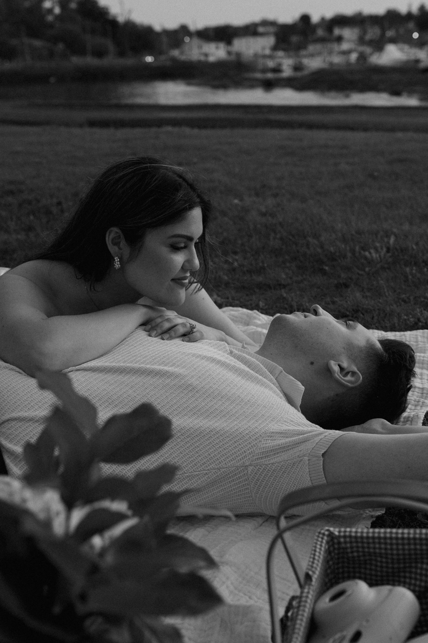 Black and white romantic portrait on picnic blanket with cityscape in distance.