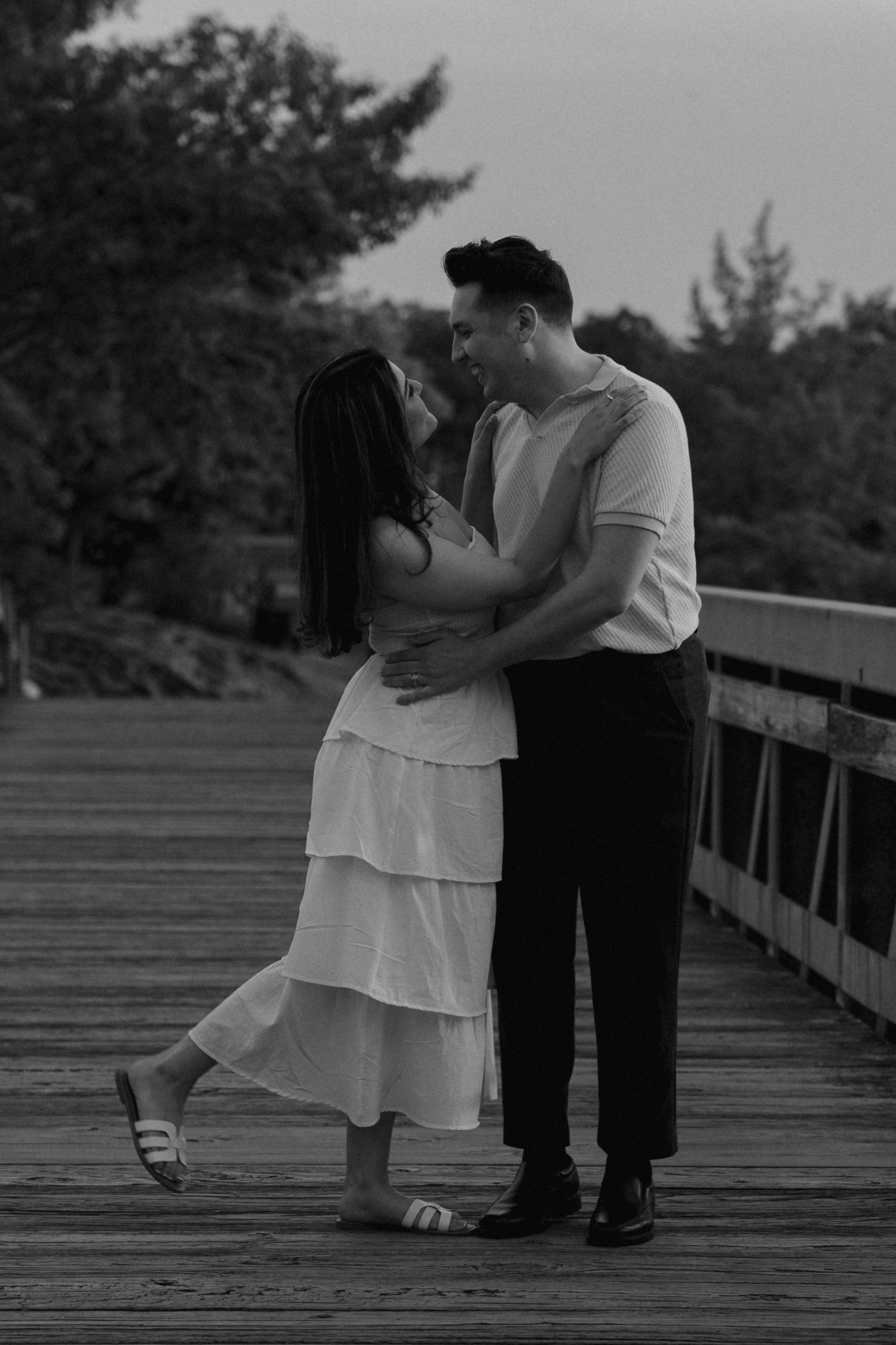 Couple in white and black attire sharing intimate moments on a wooden boardwalk.