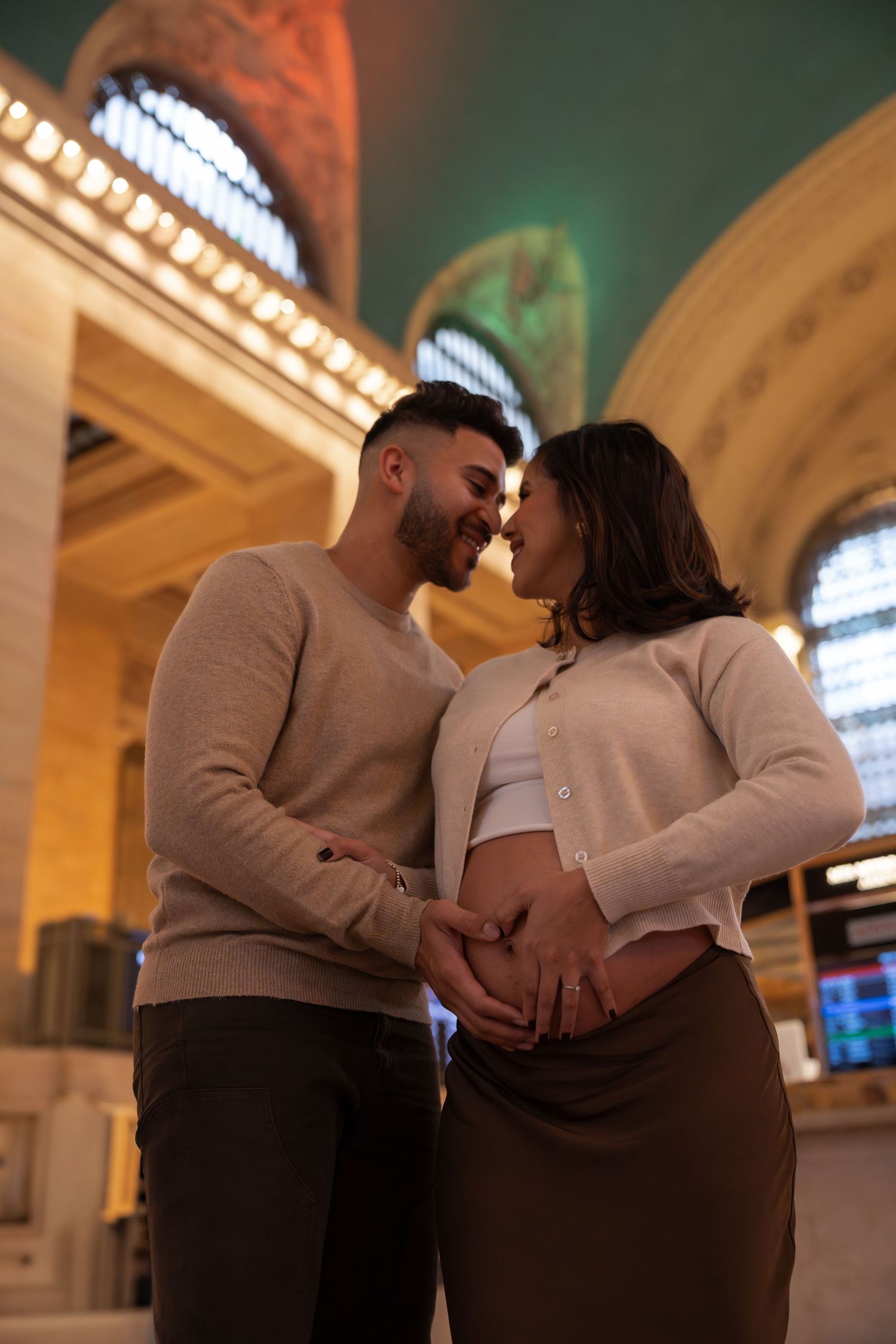 A romantic couple in matching gray and white outfits embrace in a grand architectural space with arched ceilings.