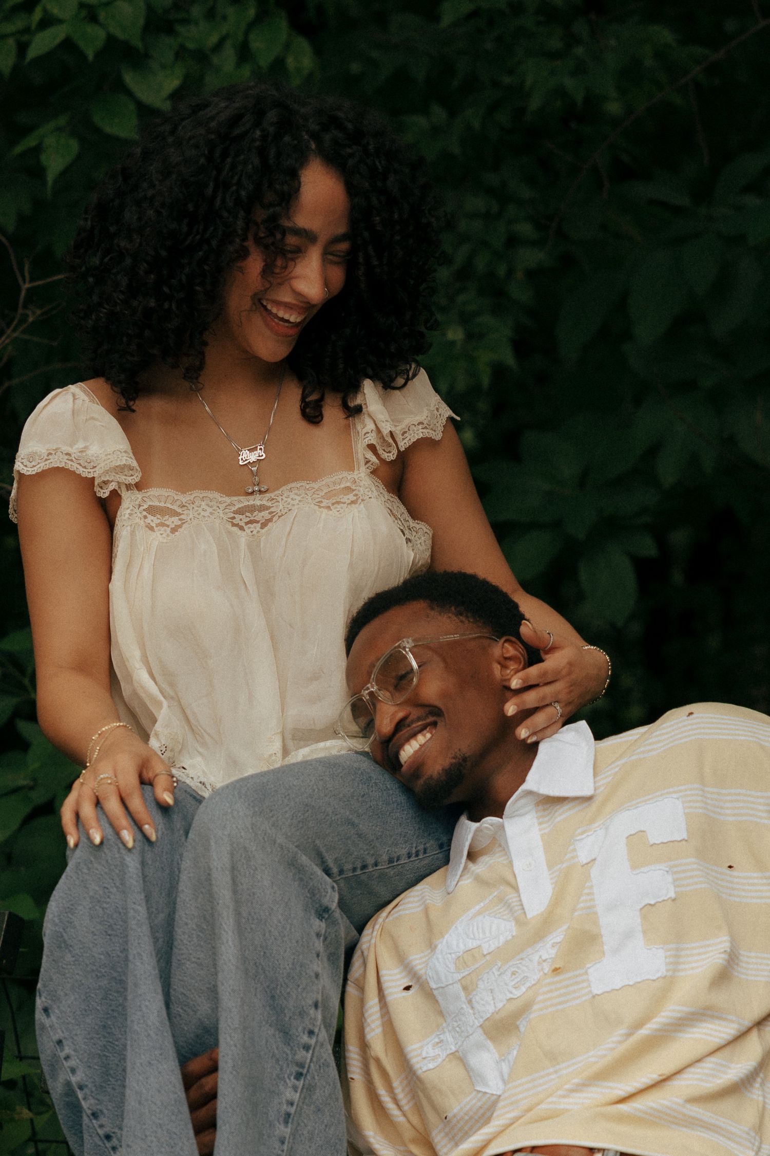 Smiling couple sharing a tender moment outdoors, woman with curly hair resting hand on mans head.