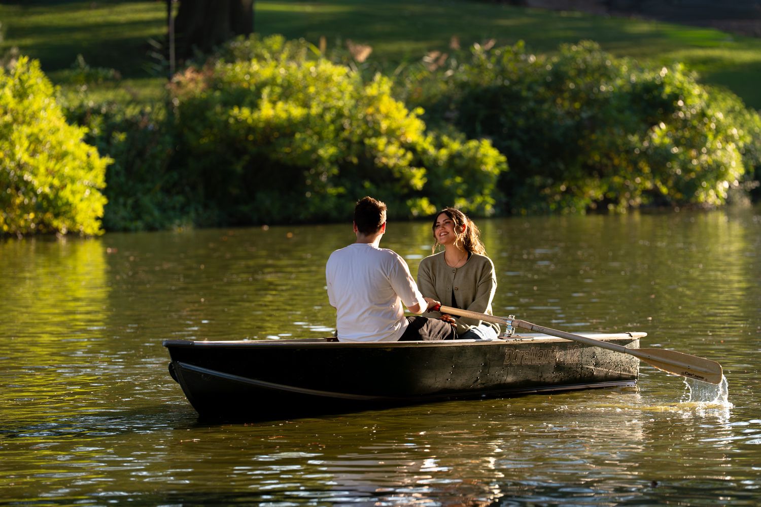 A couple enjoys a peaceful afternoon rowing on a lake surrounded by lush greenery.