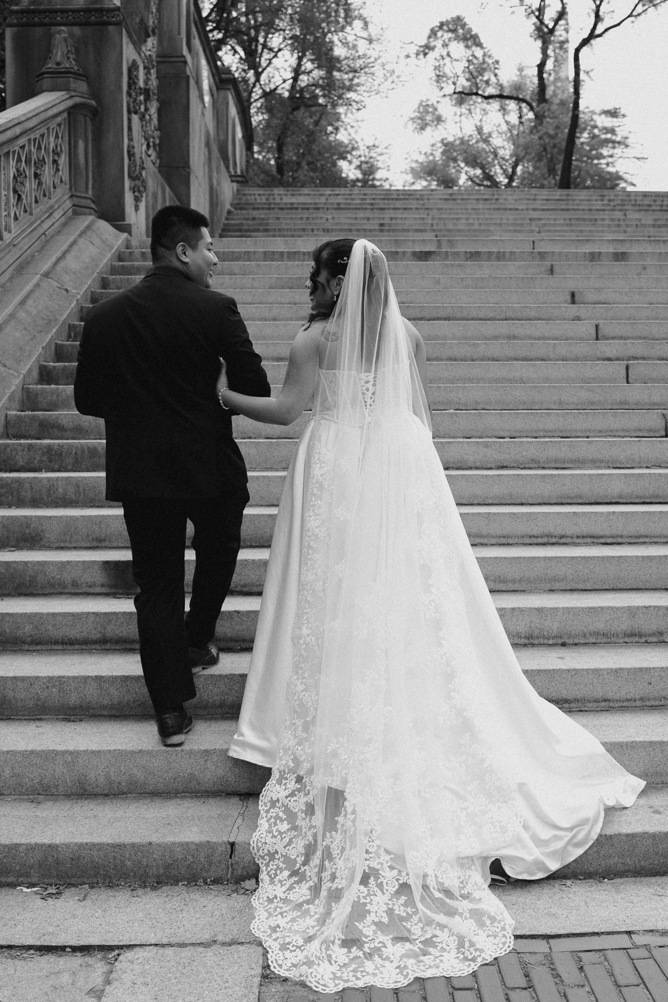 Wedding couple ascending stone steps with bride's lace dress trailing behind.