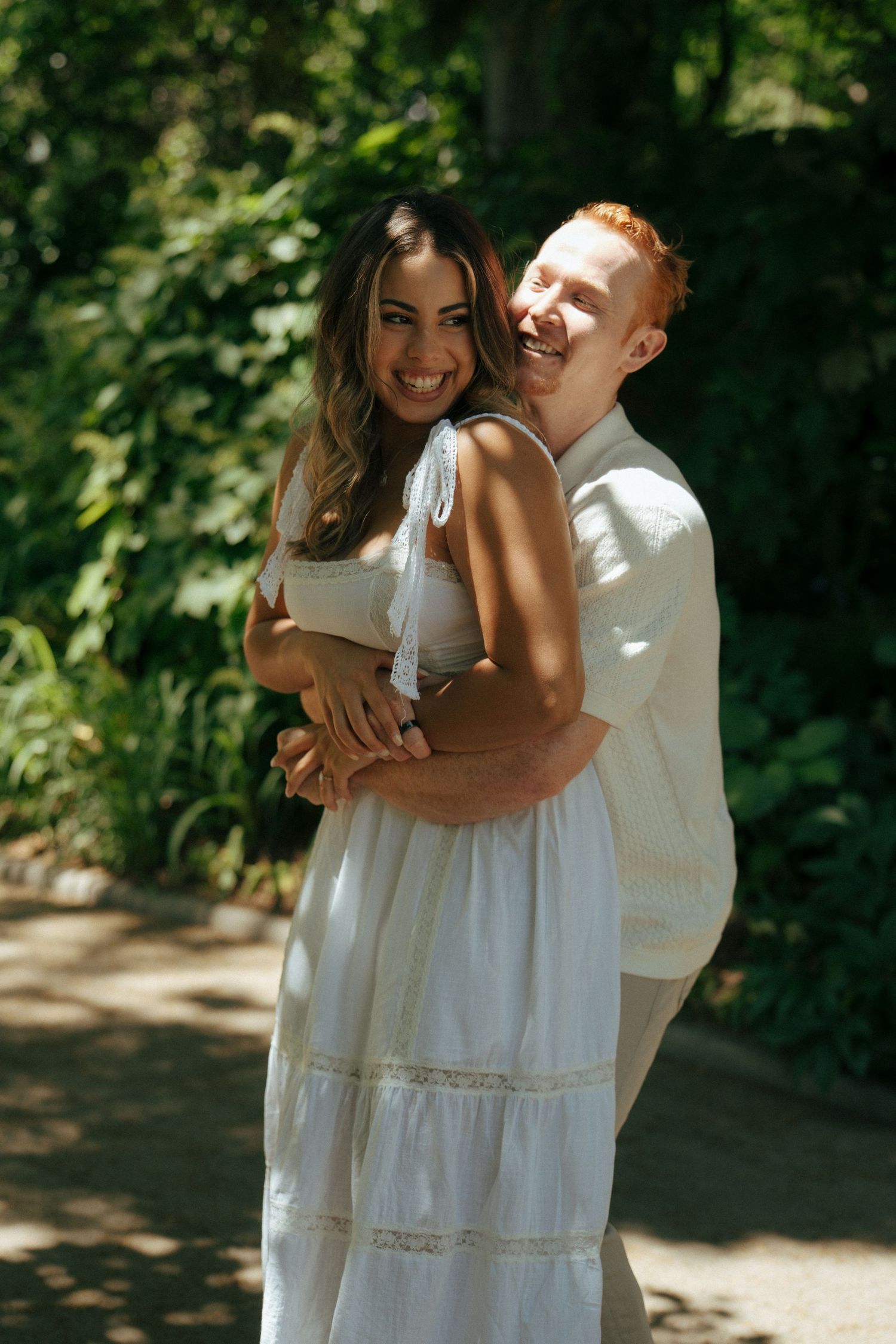 Romantic couple in white outfits embracing outdoors in a garden setting with natural lighting.