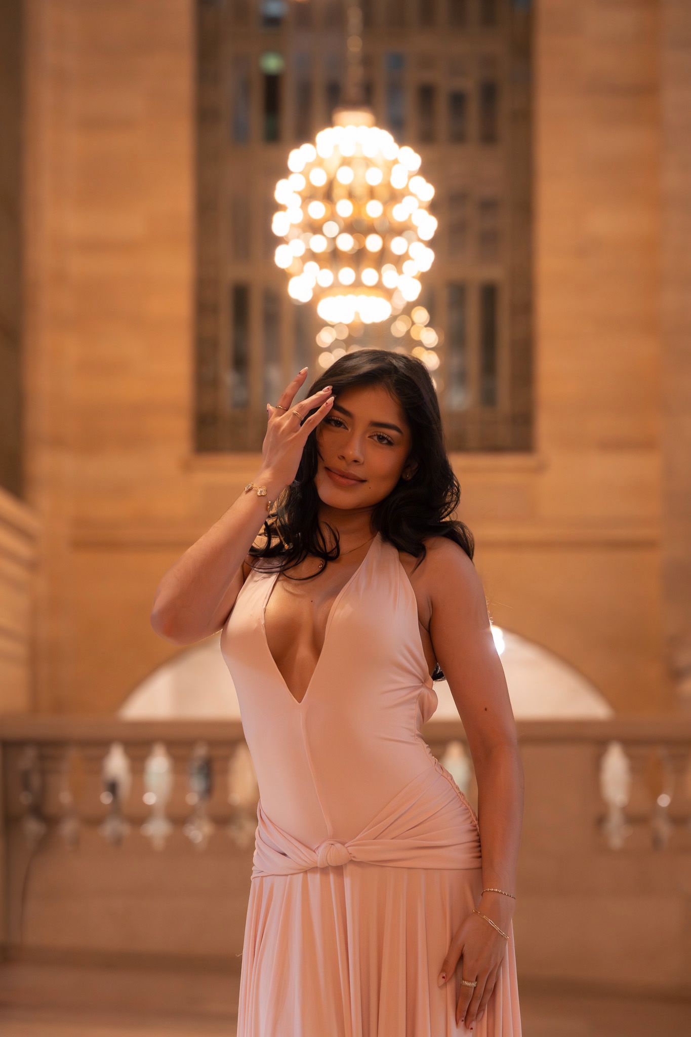 Woman in pink dress poses elegantly in front of illuminated classical architecture at dusk.