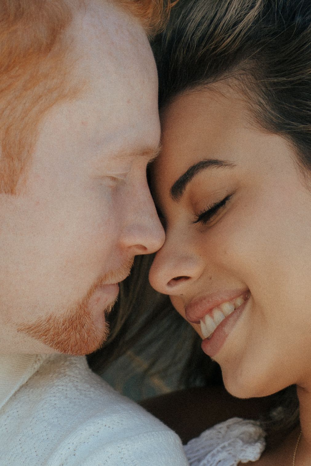 Close-up portrait of a couple sharing a tender moment against a light background.