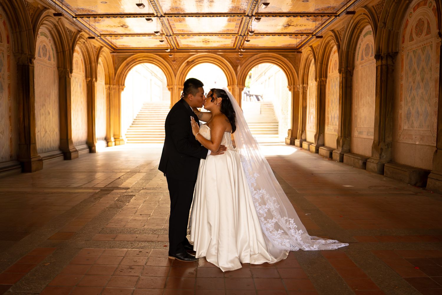 A romantic wedding portrait under golden arches with dramatic lighting and a long lace veil.