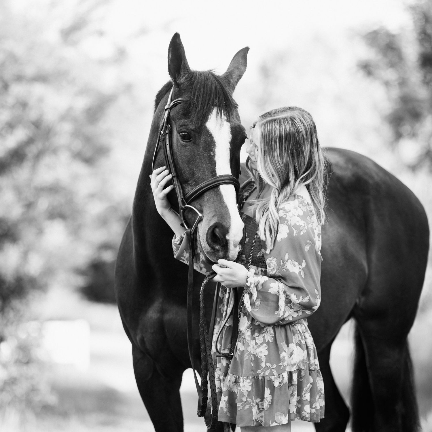 Tender moment between a dark horse and person in a floral dress captured in black and white.