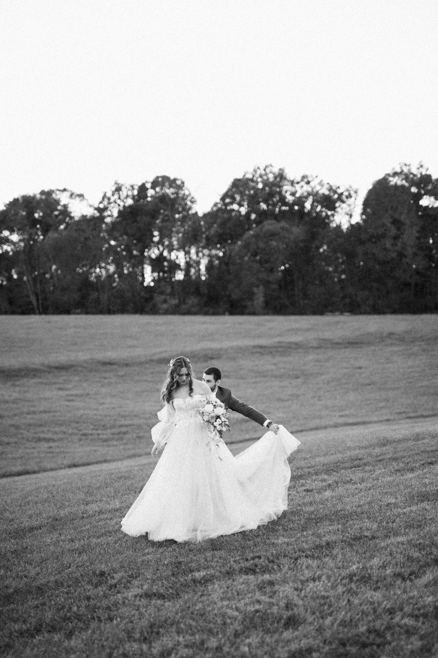 A bride and groom twirl together on a grassy field in black and white.