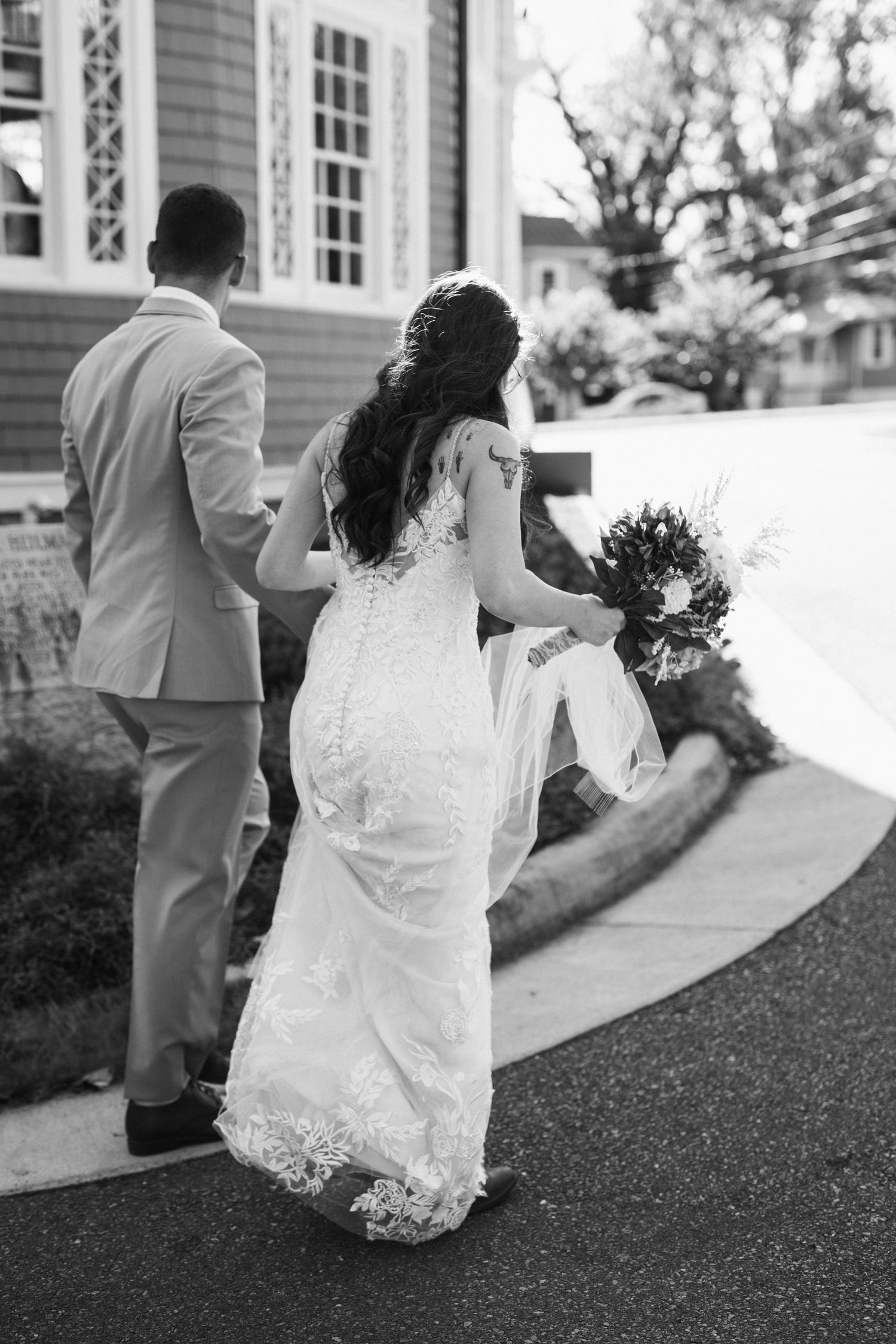 A couple walks along a curved pathway outside a traditional building in formal attire.