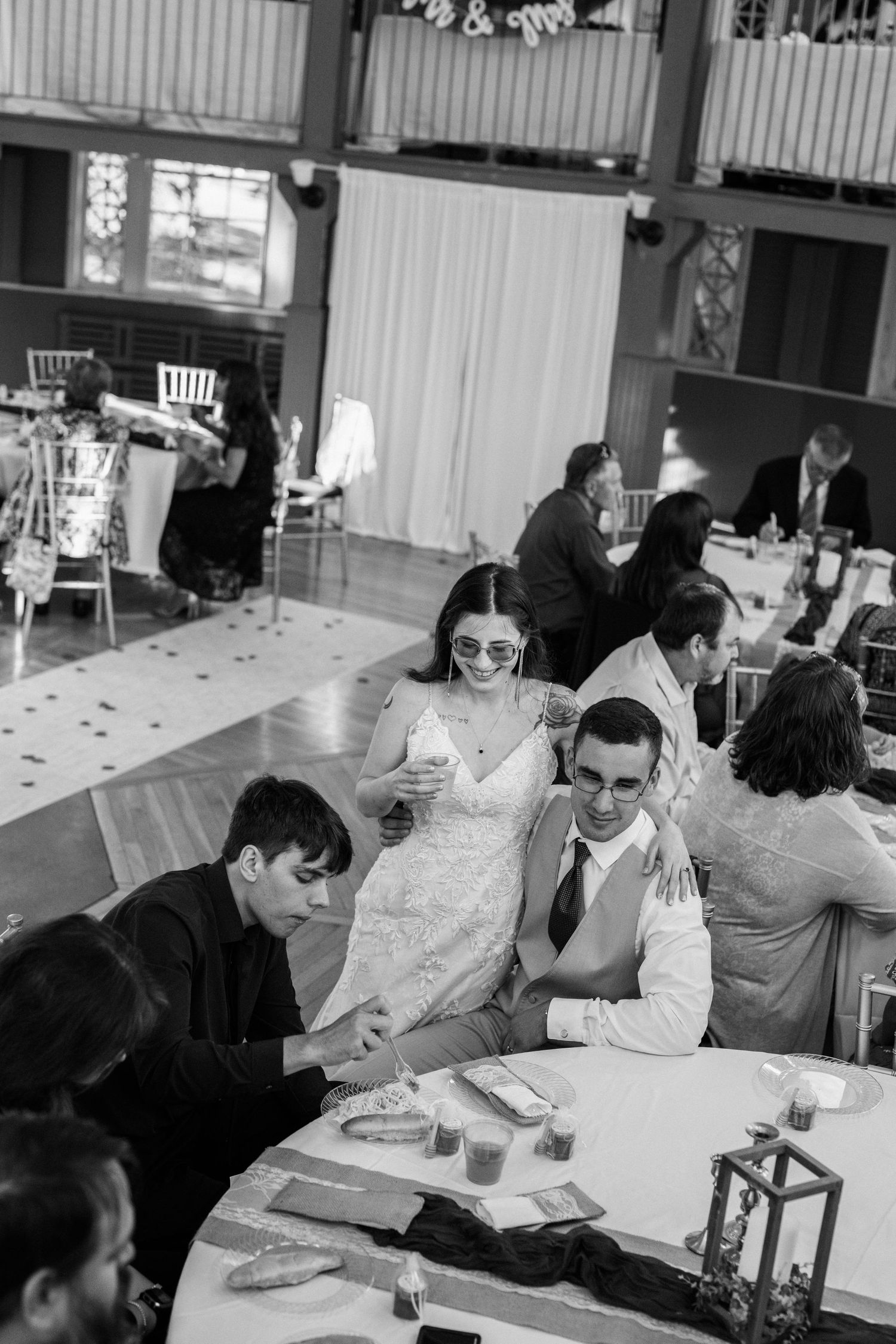 Black and white reception photo showing guests gathered at tables during wedding celebration.