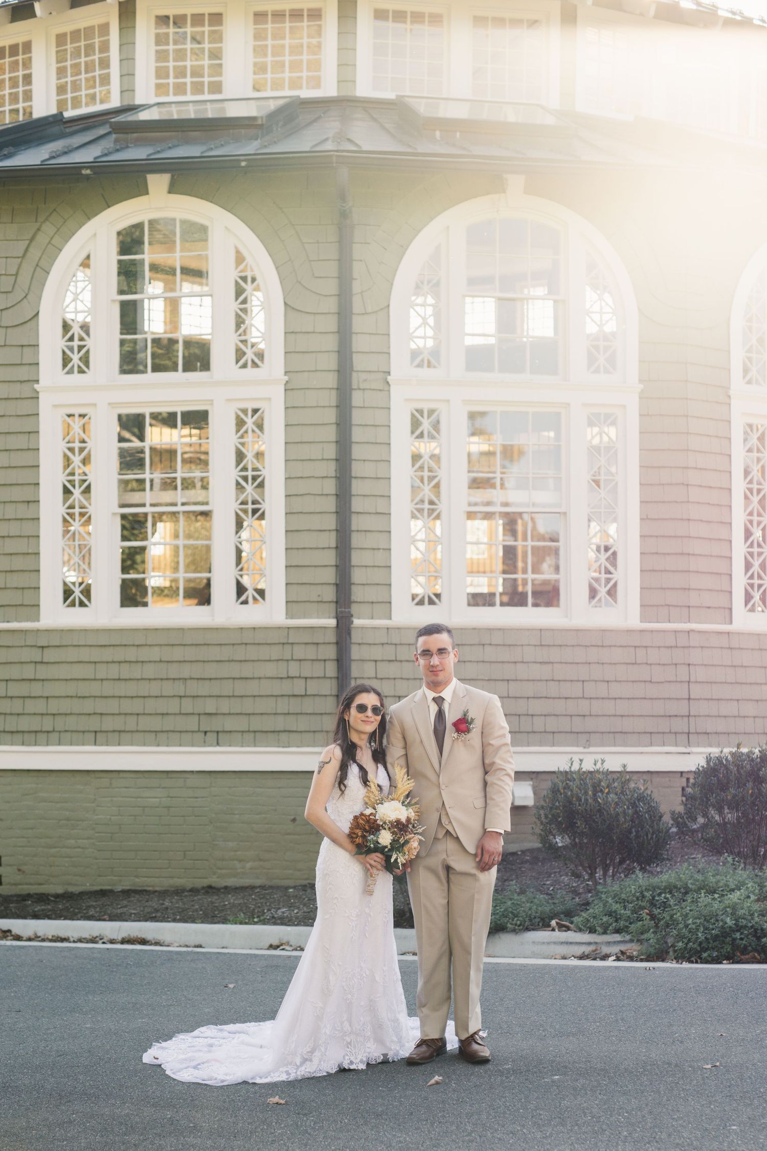 A wedding couple poses in front of a historic building with arched windows and elegant architecture.