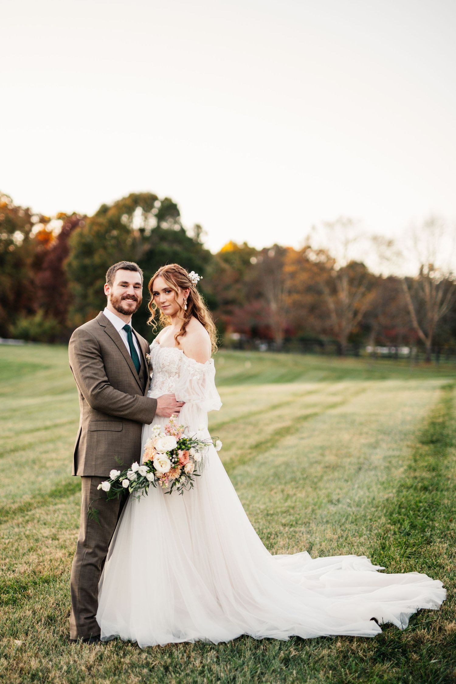 A wedding couple embraces in an autumn field during golden hour.