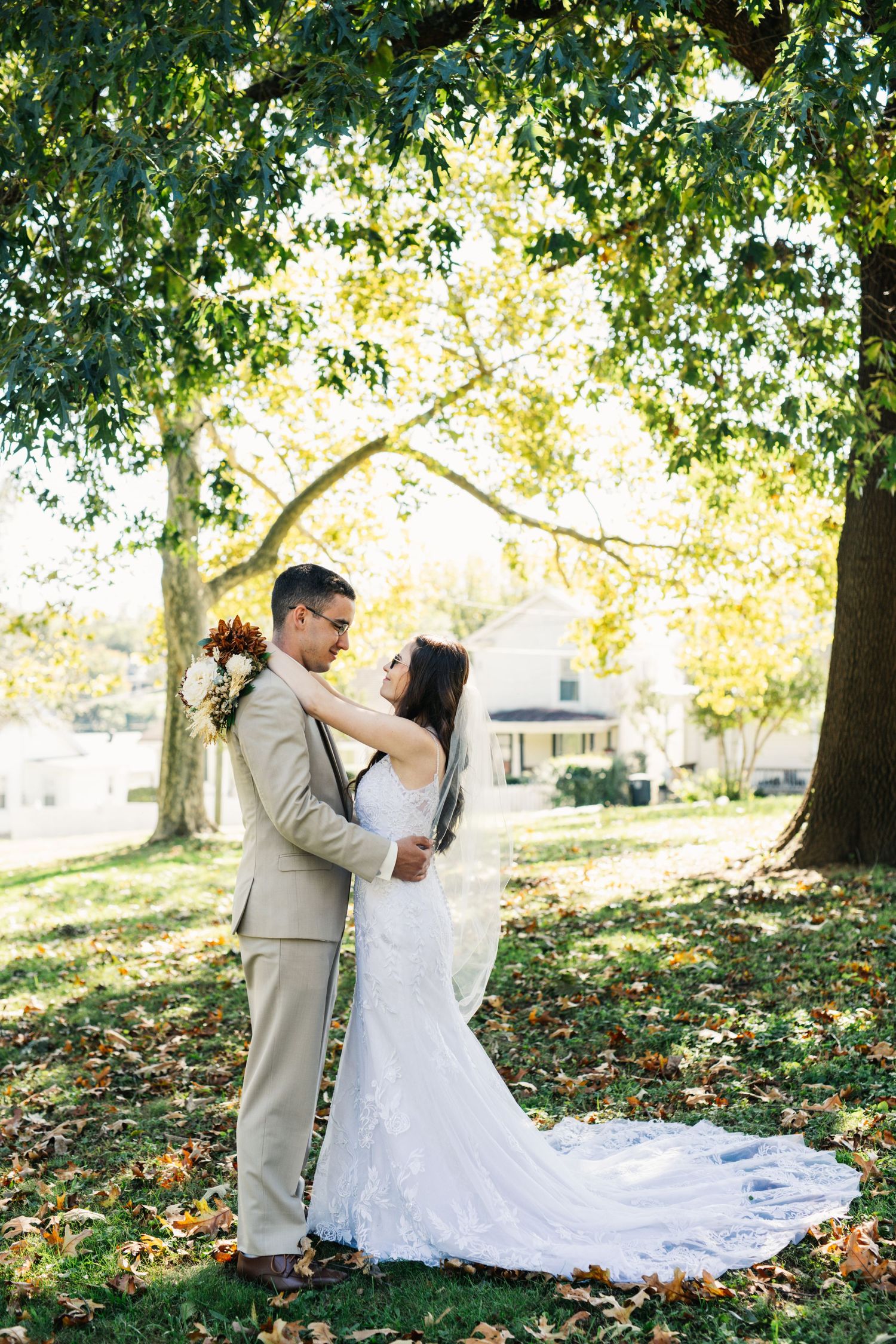 A romantic wedding portrait captured under tall trees with golden autumn light.