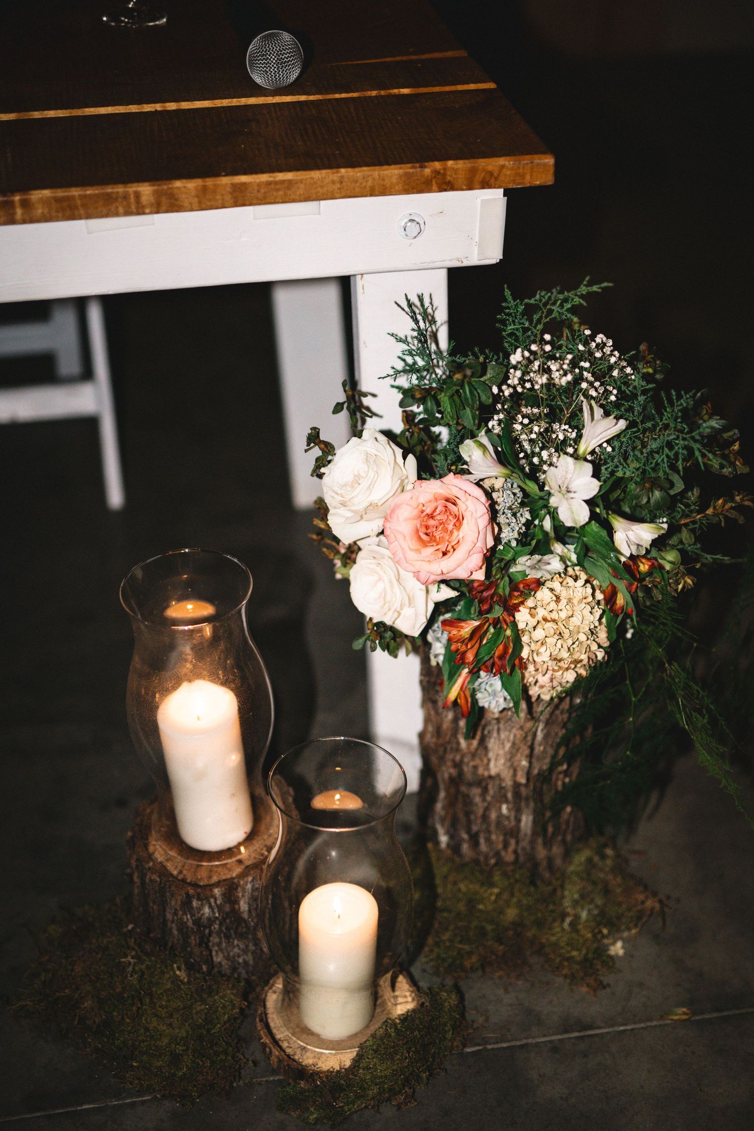 Wedding reception decor featuring glass hurricane candles on wood slices with a floral arrangement.