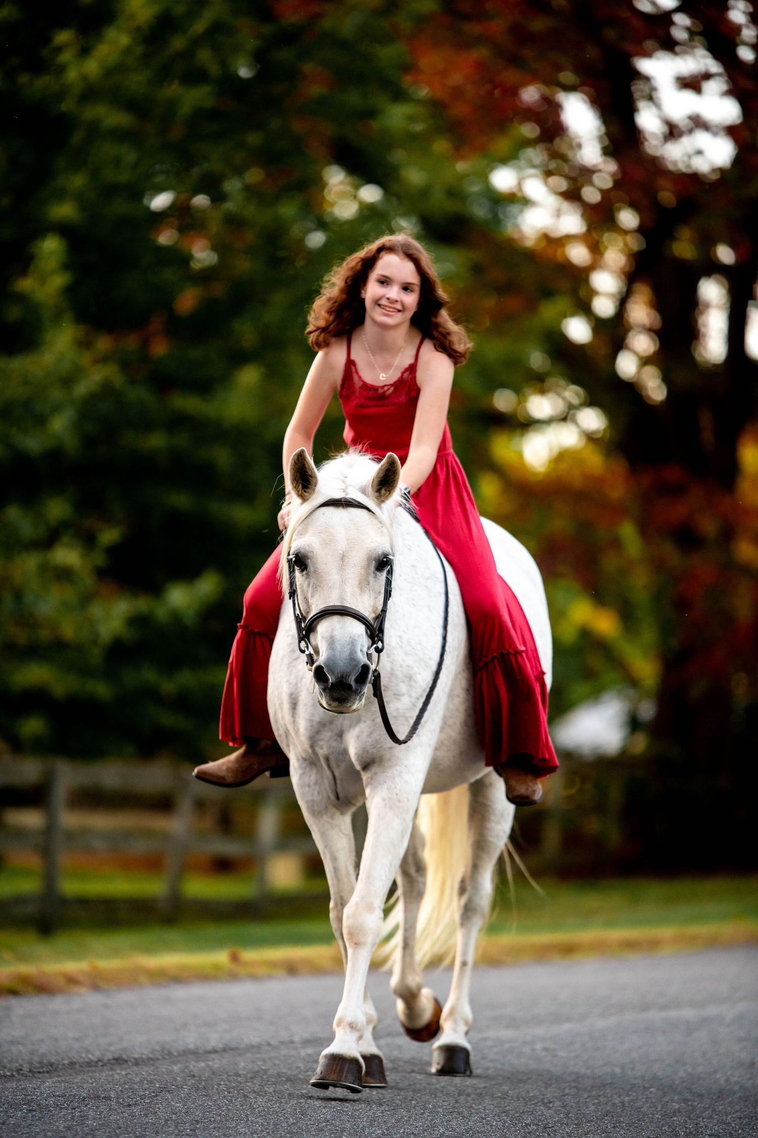 Girl in a red dress rides a white horse along an autumn road during sunset.
