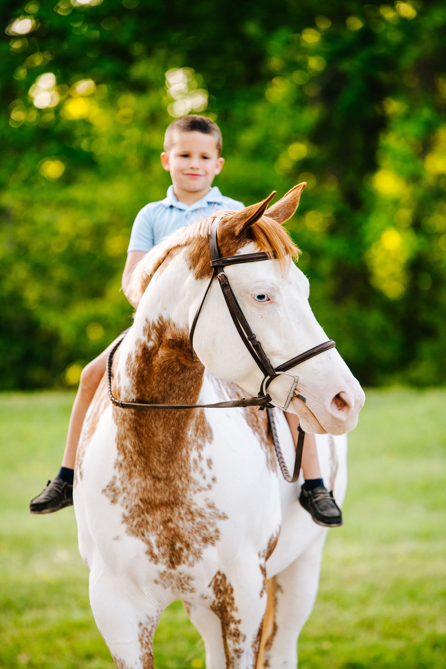 Child rides paint horse with brown patches in green summer field.