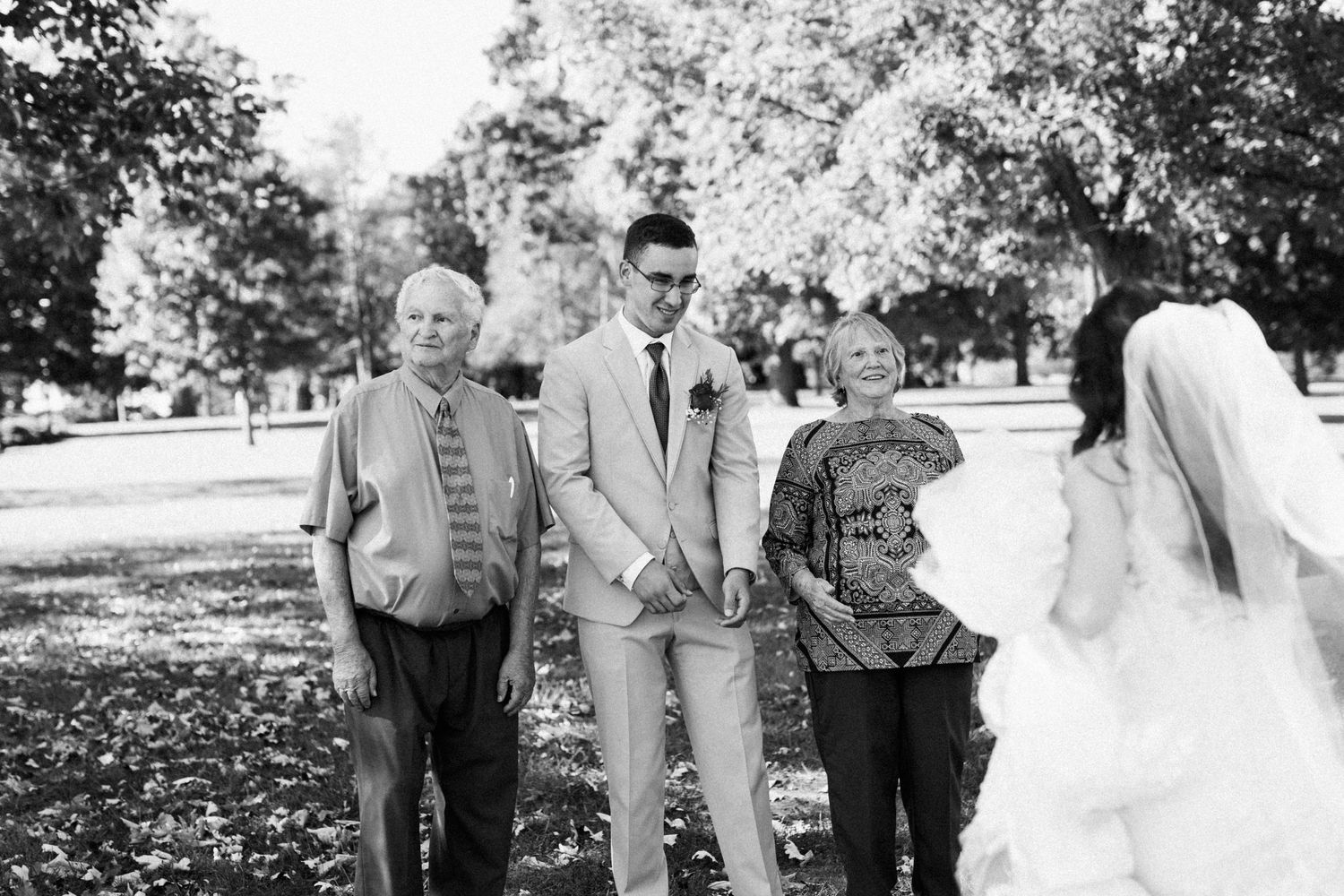 Black and white photo of a small wedding party gathering outdoors under trees.