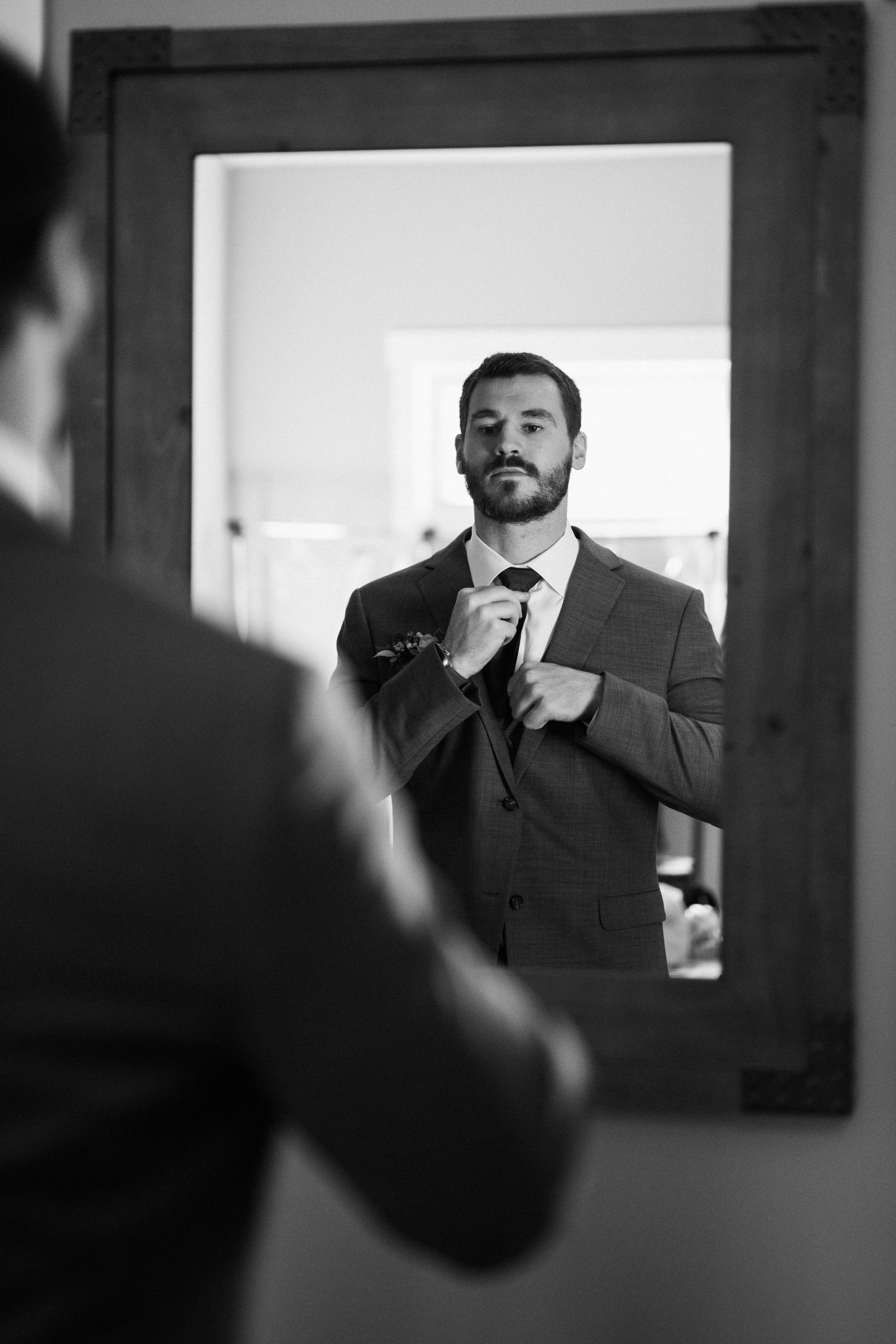 Black and white reflection of someone adjusting a tie in a mirror.