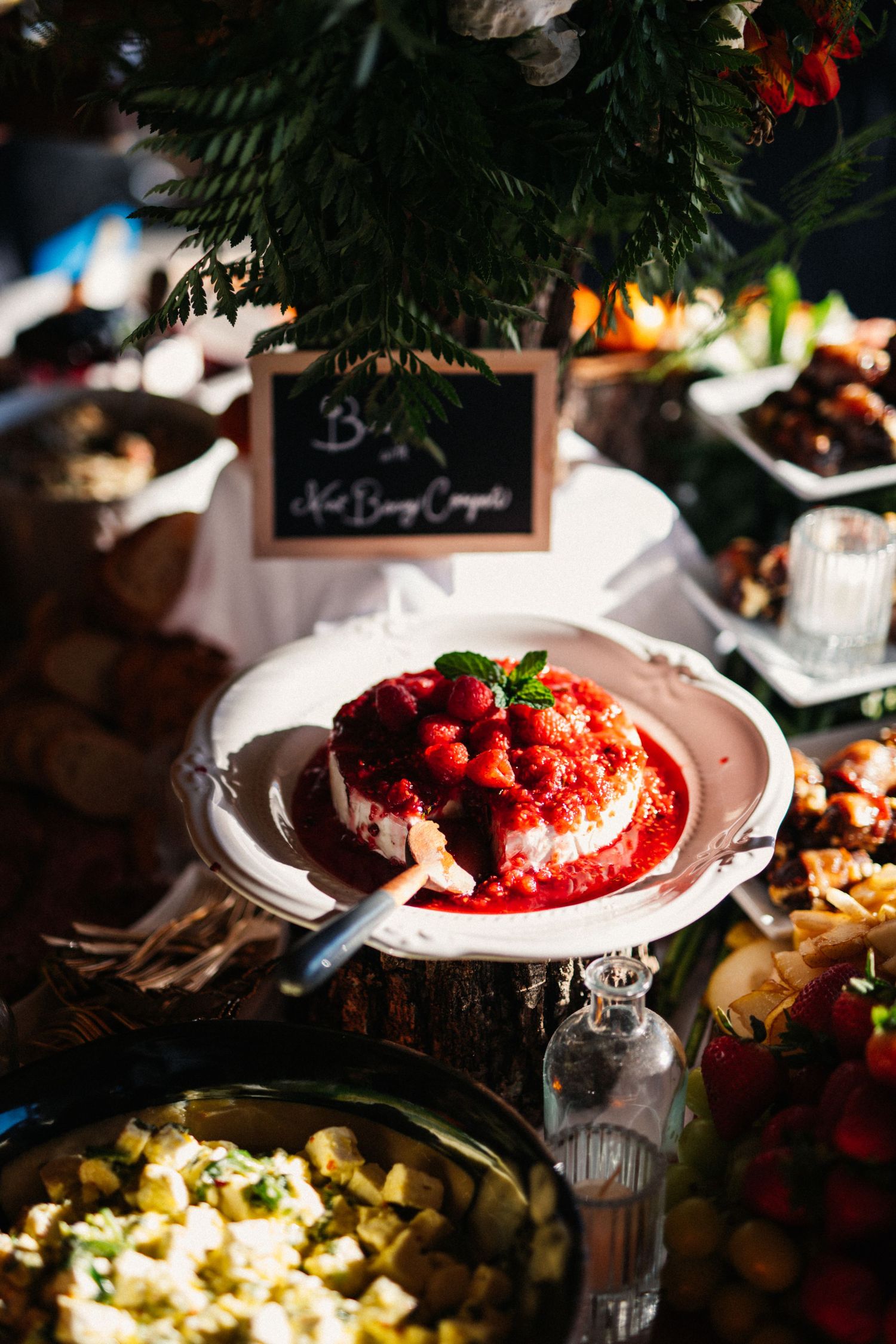 Elegant dessert plate with red berries and sauce in a rustic wedding reception setting.