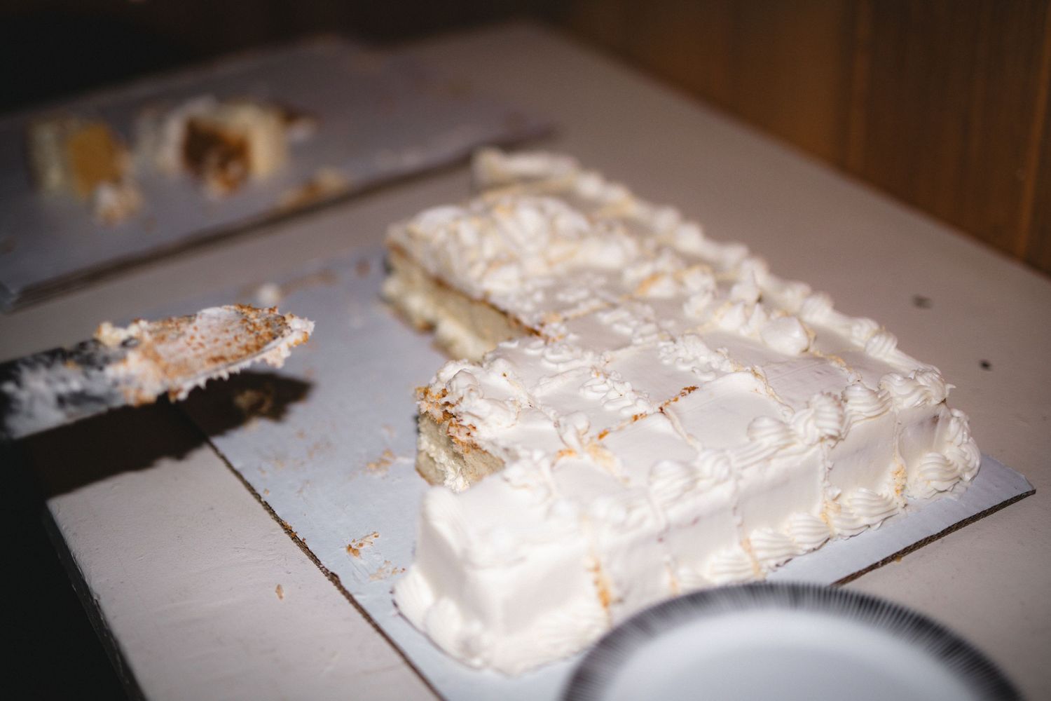 A partially eaten white wedding cake with messy slices cut on a silver platter.