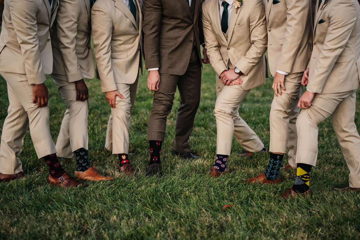 Groomsmen in khaki suits show off their colorful socks while standing on grass.