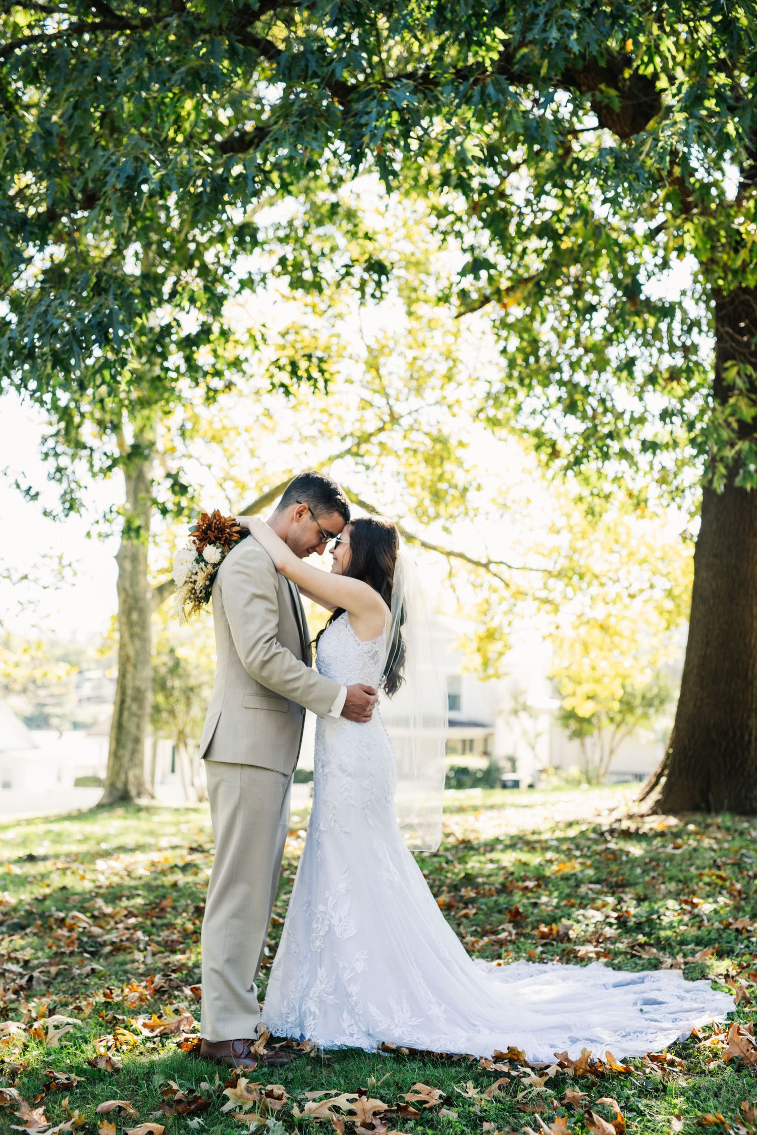 A romantic wedding portrait under fall trees with golden sunlight filtering through leaves.